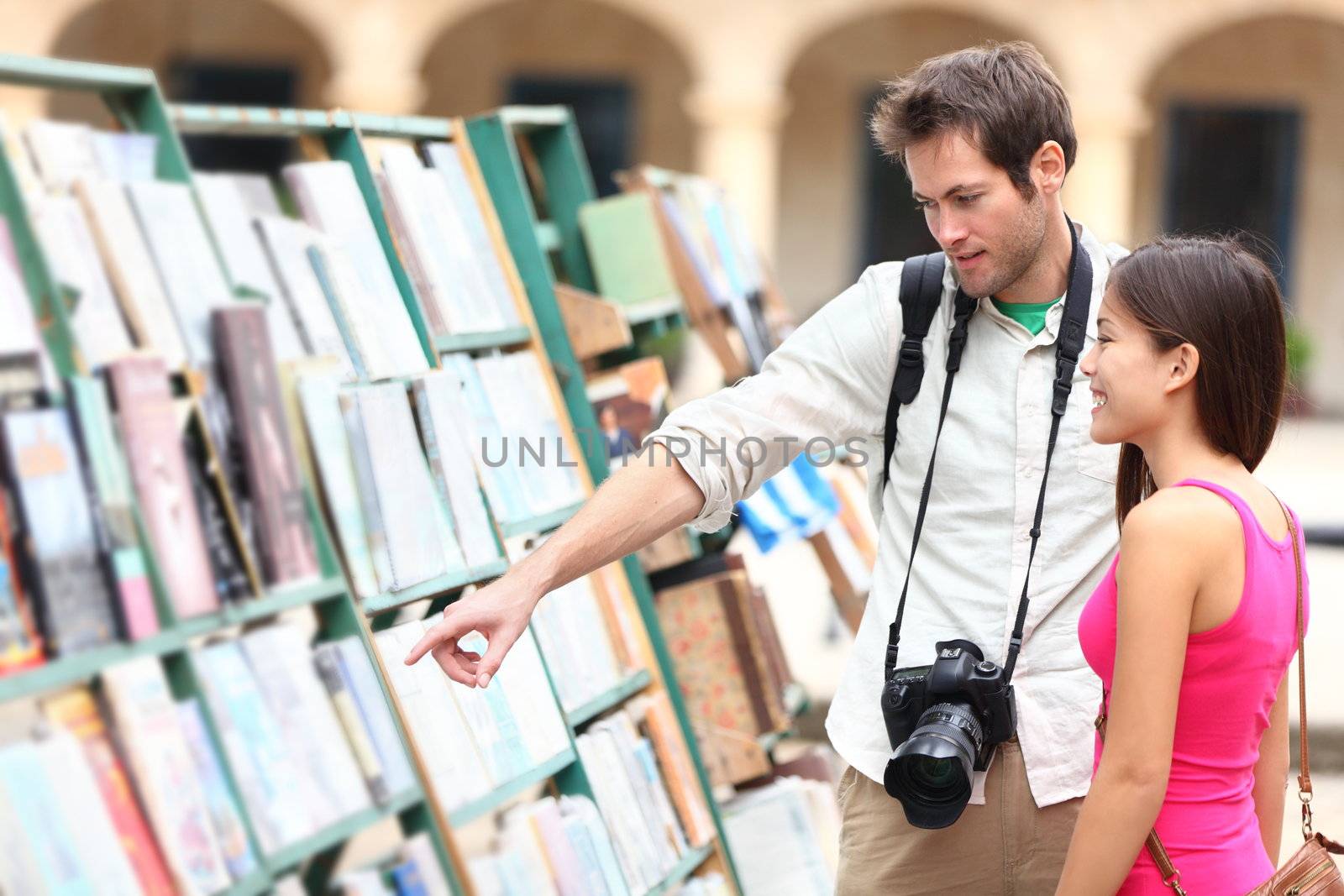 Tourist couple in Havana, Cuba looking at books together having fun on vacation travel on Plaza de Armas in Old Havana. Young travelers interracial couple, Asian woman, Caucasian man.