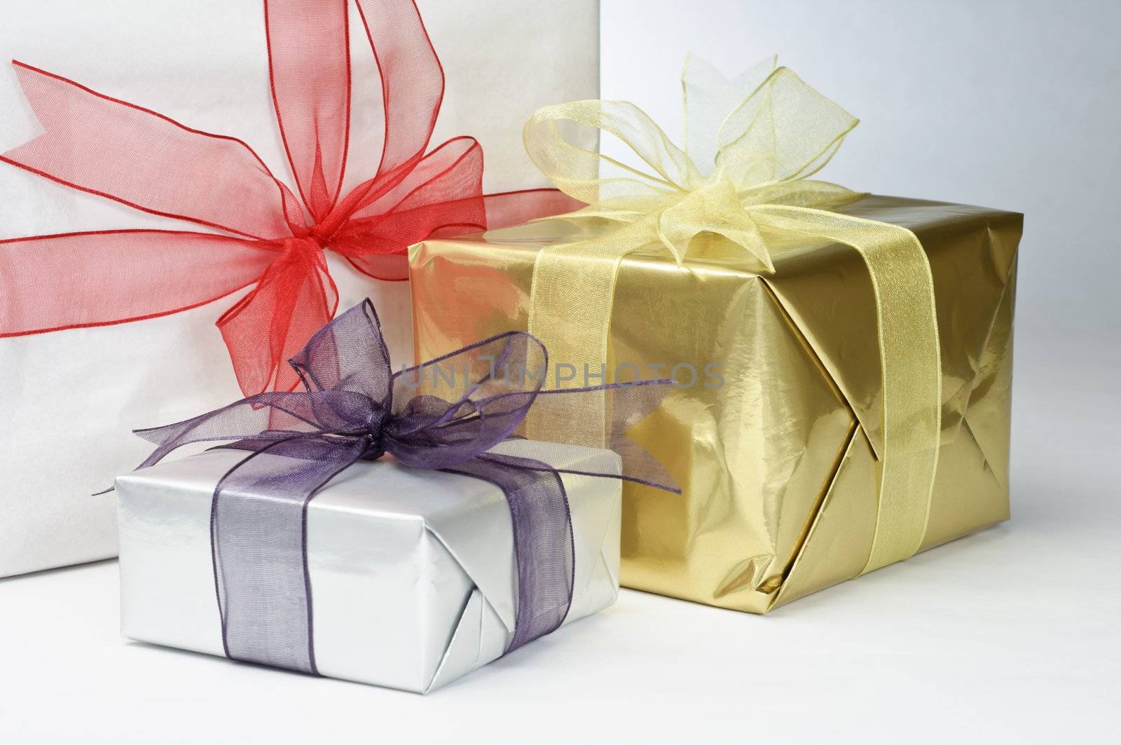 Close up of three gifts, wrapped in white and metallic foil papers, tied with ribbons and knotted with bows.