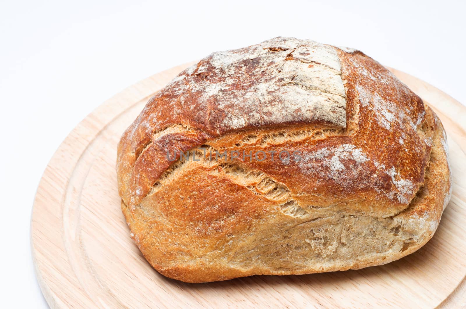 Elevated view of a fresh, uncut loaf of bread, resting on a light wood chopping board.