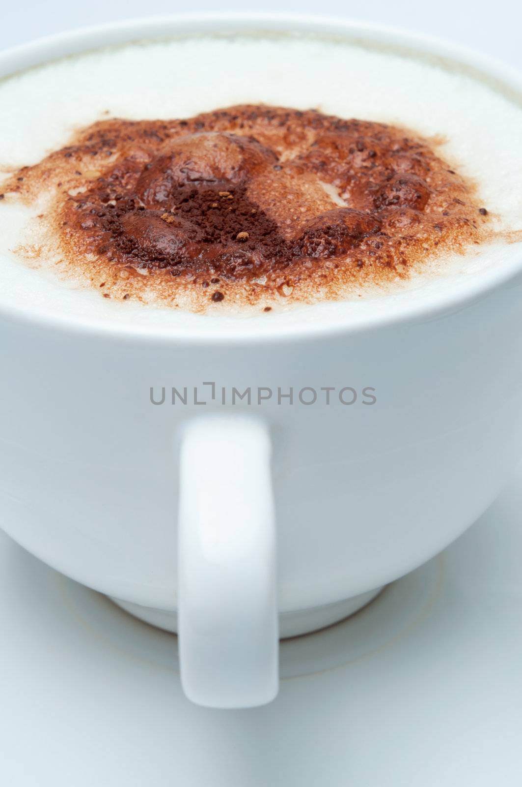 Close up of a cup of coffee with frothed milk and cocoa sprinkles, with cup handle facing front.