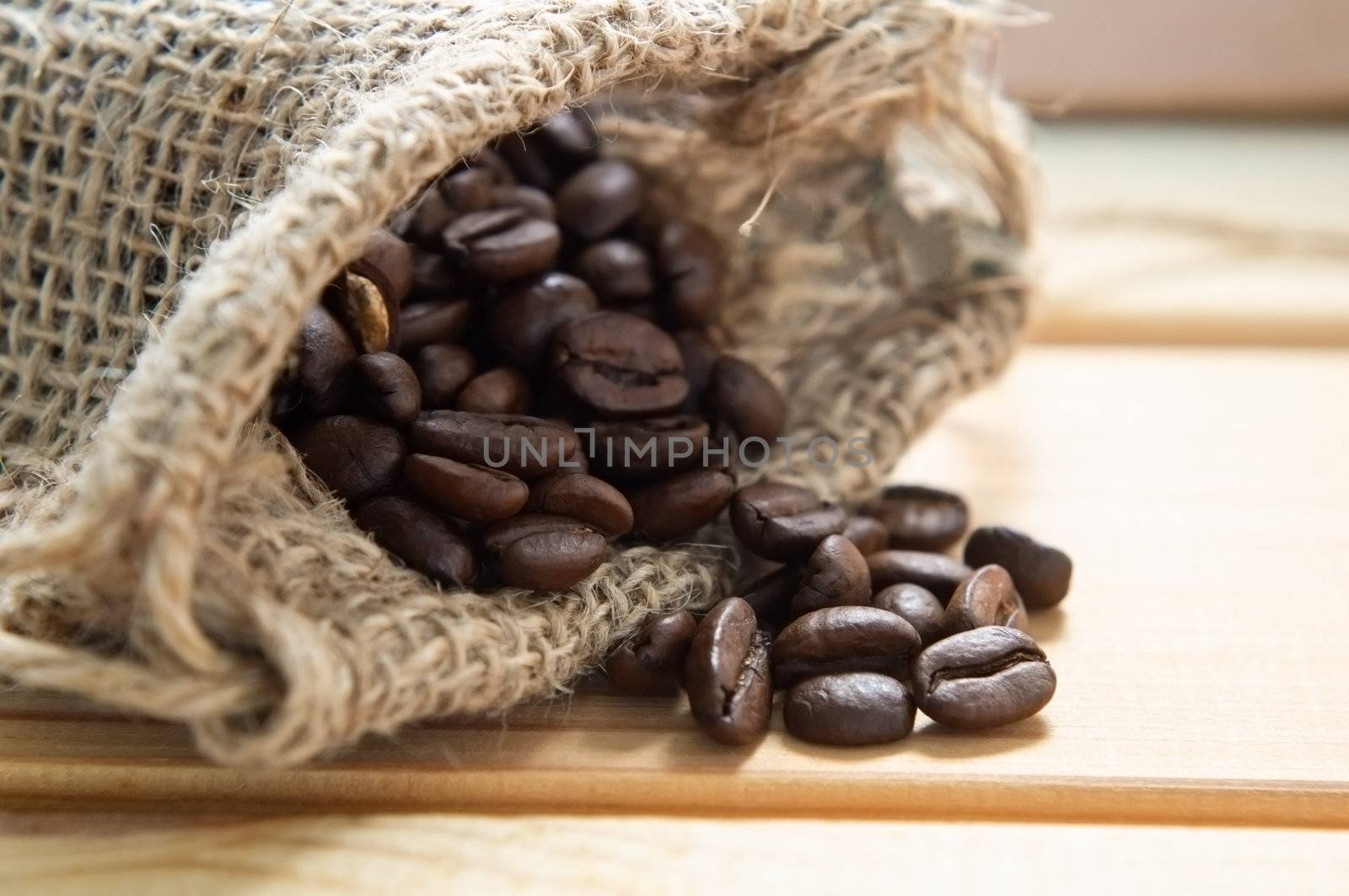 Close up of a hessian sack containing whole coffee beans, spilling on to wooden table.