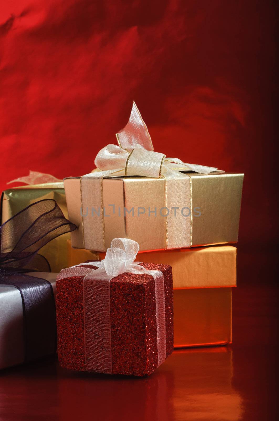 A selection of gift packages, tied with ribbons, against a foil red background.  Vertical (portrait) orientation.