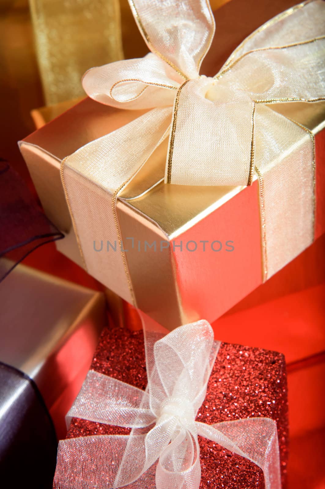 A pile of Christmas gifts, in shiny and sparkly packaging, tied in ribbosns with bows on a red reflective surface.  Portrait (vertical) orientation.