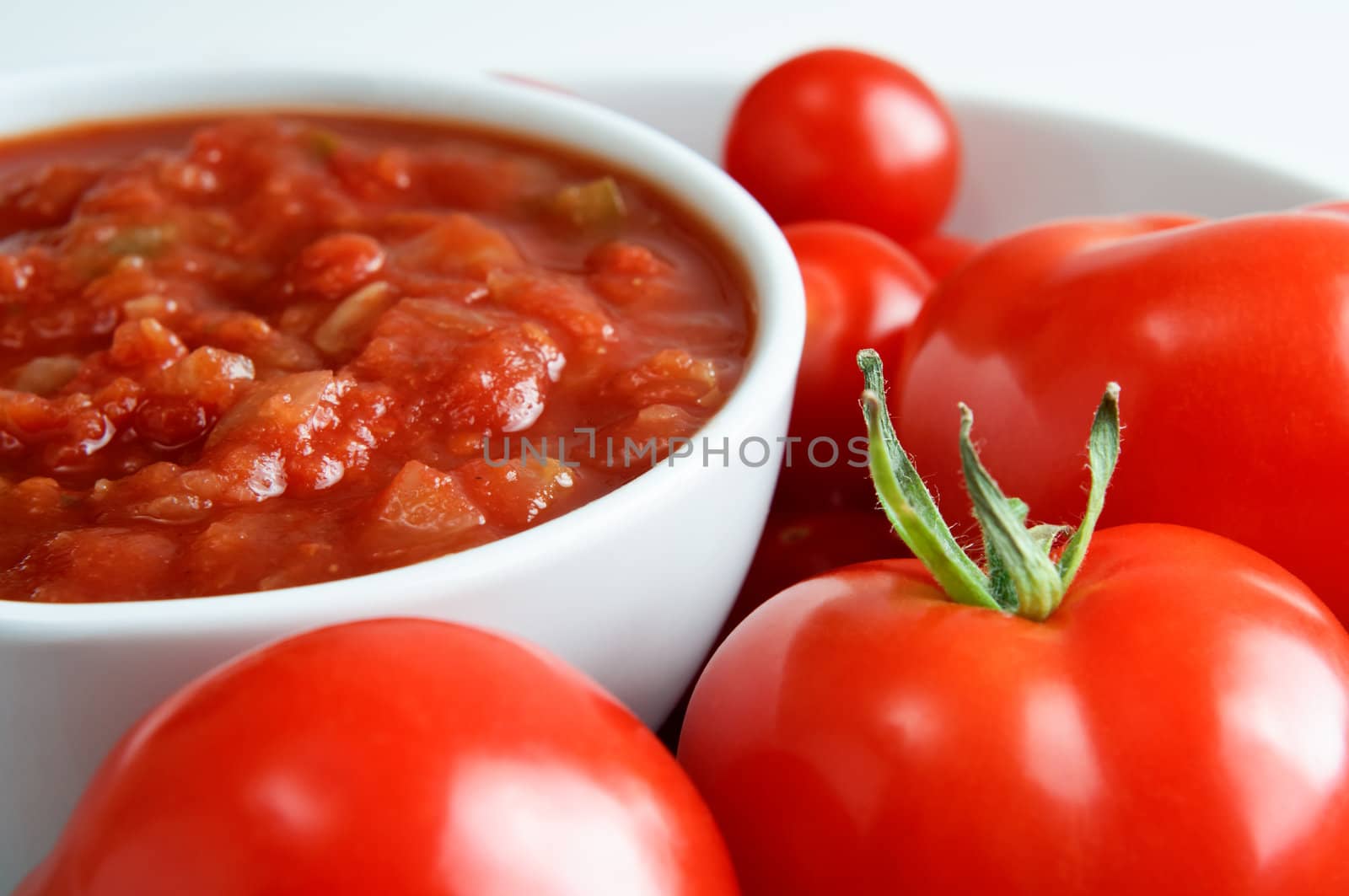 A white china bowl of red salsa, surrounded by fresh tomatoes.  Landscape (horizontal) orientation. 