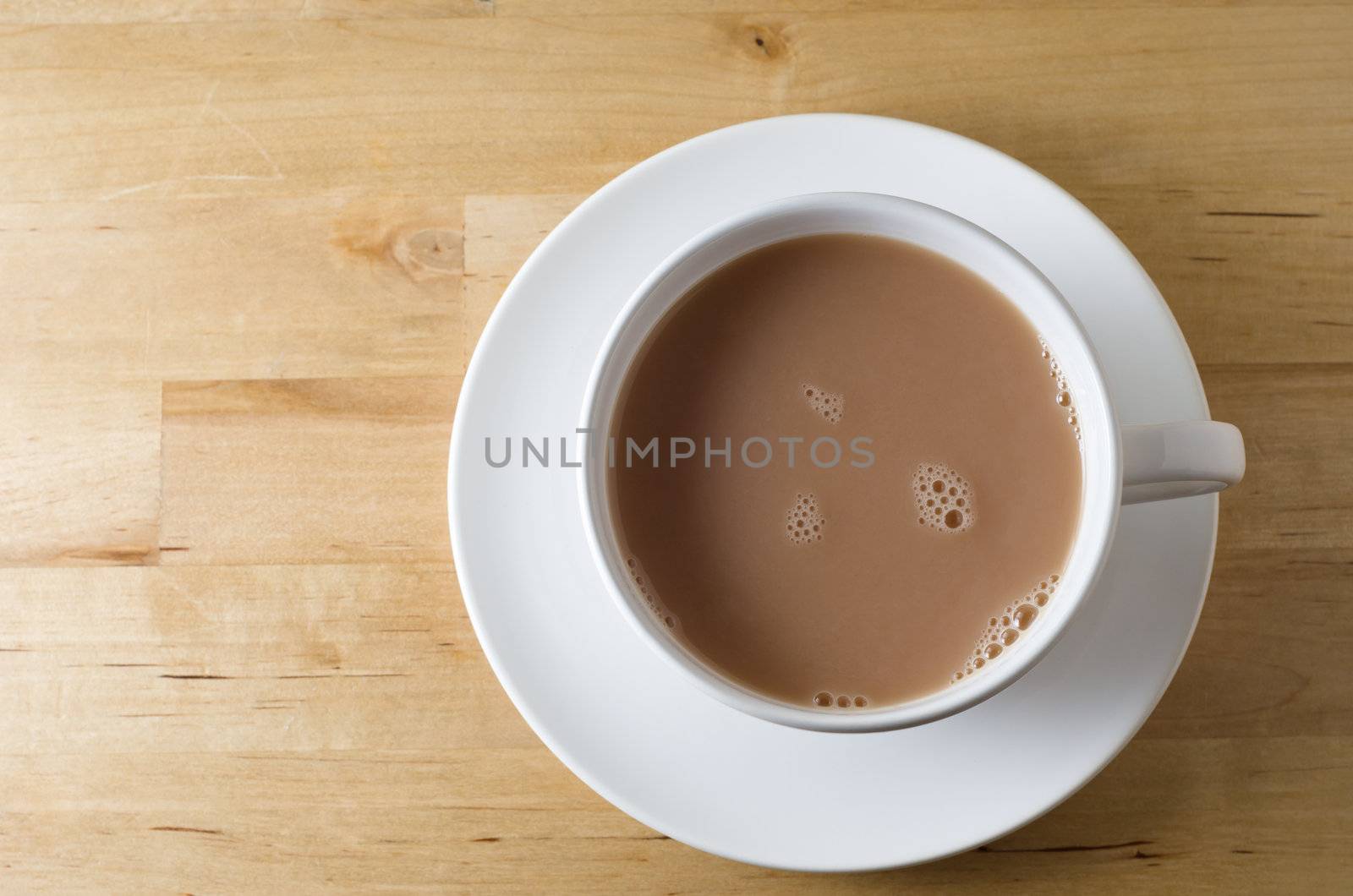 Overhead shot of a cup of tea, with saucer on old, scratched light wooden table with copy space to left.  Landscape (horizontal) orientation.