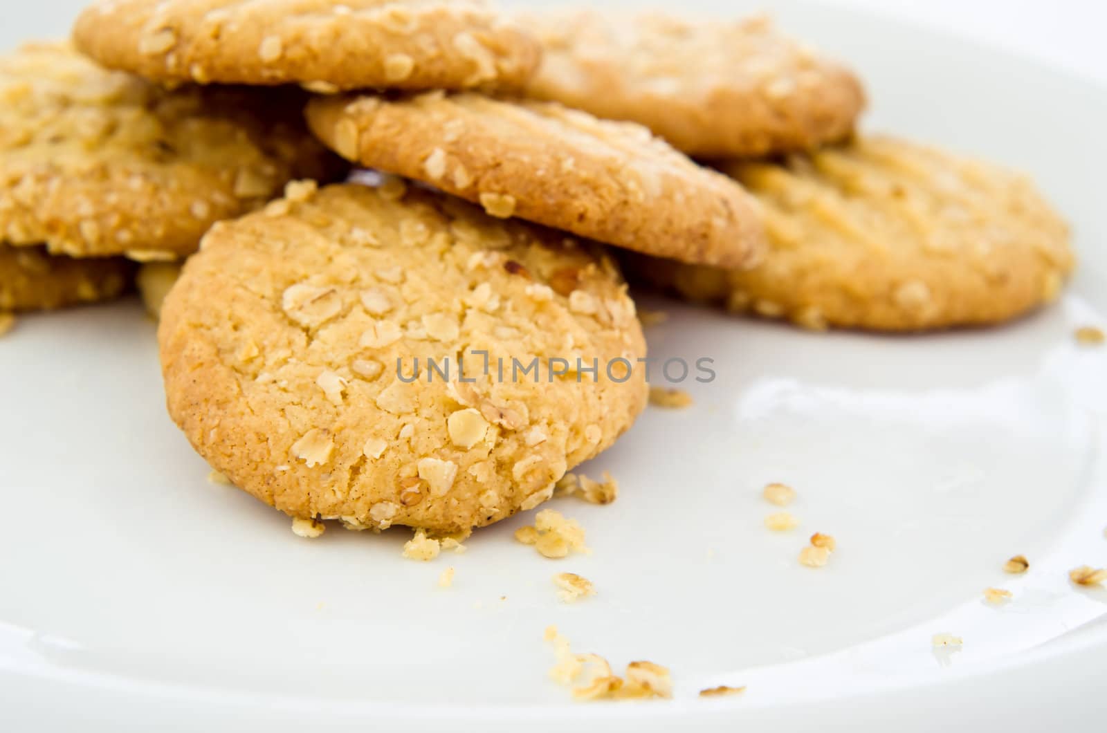 A white plate of freshly baked crumbly oat biscuits (cookies), with crumbs.