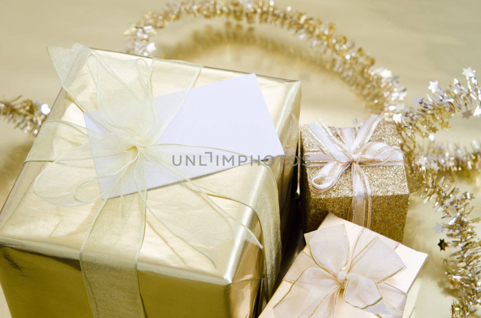 A group of Christmas gifts wrapped in gold foil paper with ribbon on a gold reflective surface with tinsel garland in background.