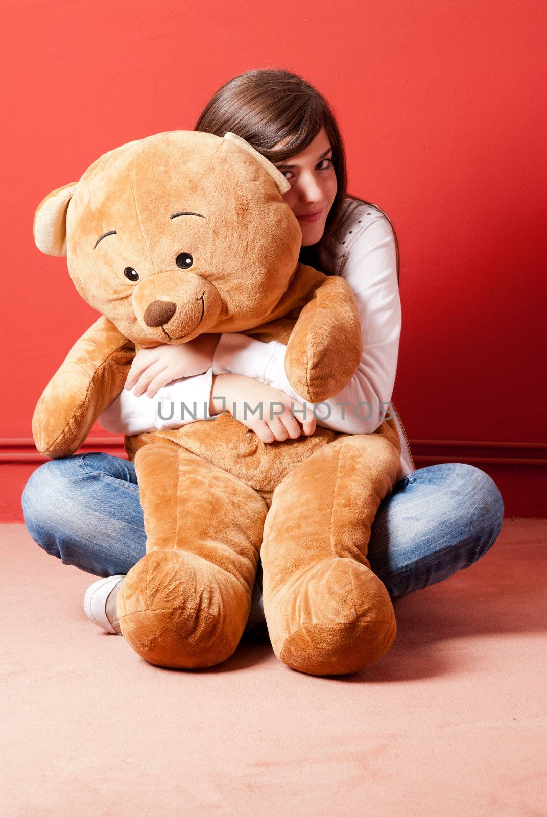 Young woman embracing teddy bear sitting on floor by dgmata