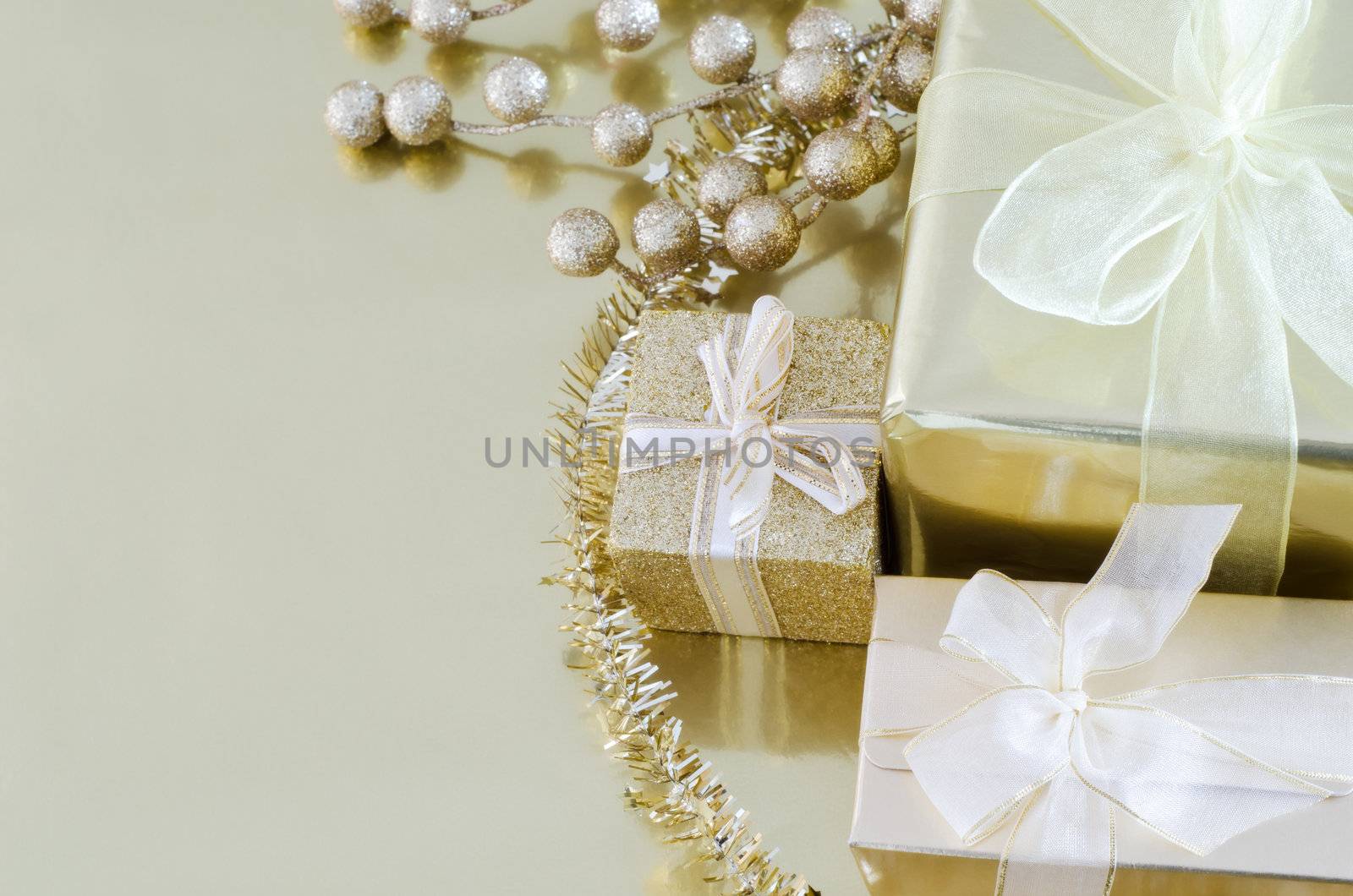 Wrapped and tied Christmas gifts and decorations in shiny gold on reflective surface with copy space to left.