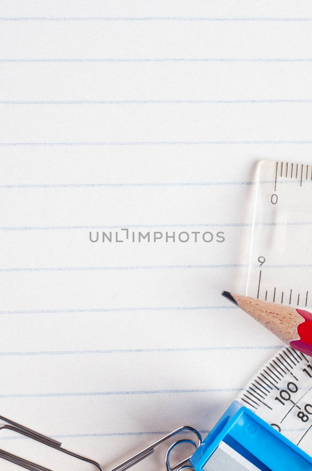 A selection of stationery bordering the bottom and right side of a lined paper background from a school exercise book.