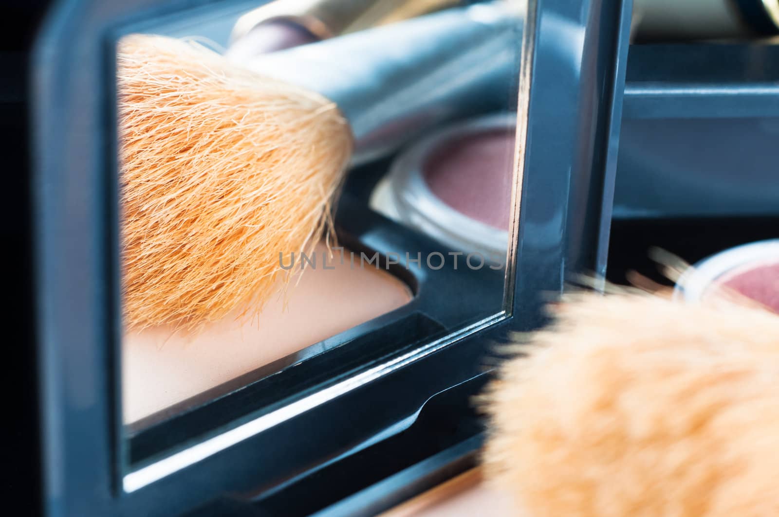 An open powder compact, with cosmetic brush and make up items reflected in it's mirror.  Focus is on the reflection.  Close up (macro) in landscape orientation.