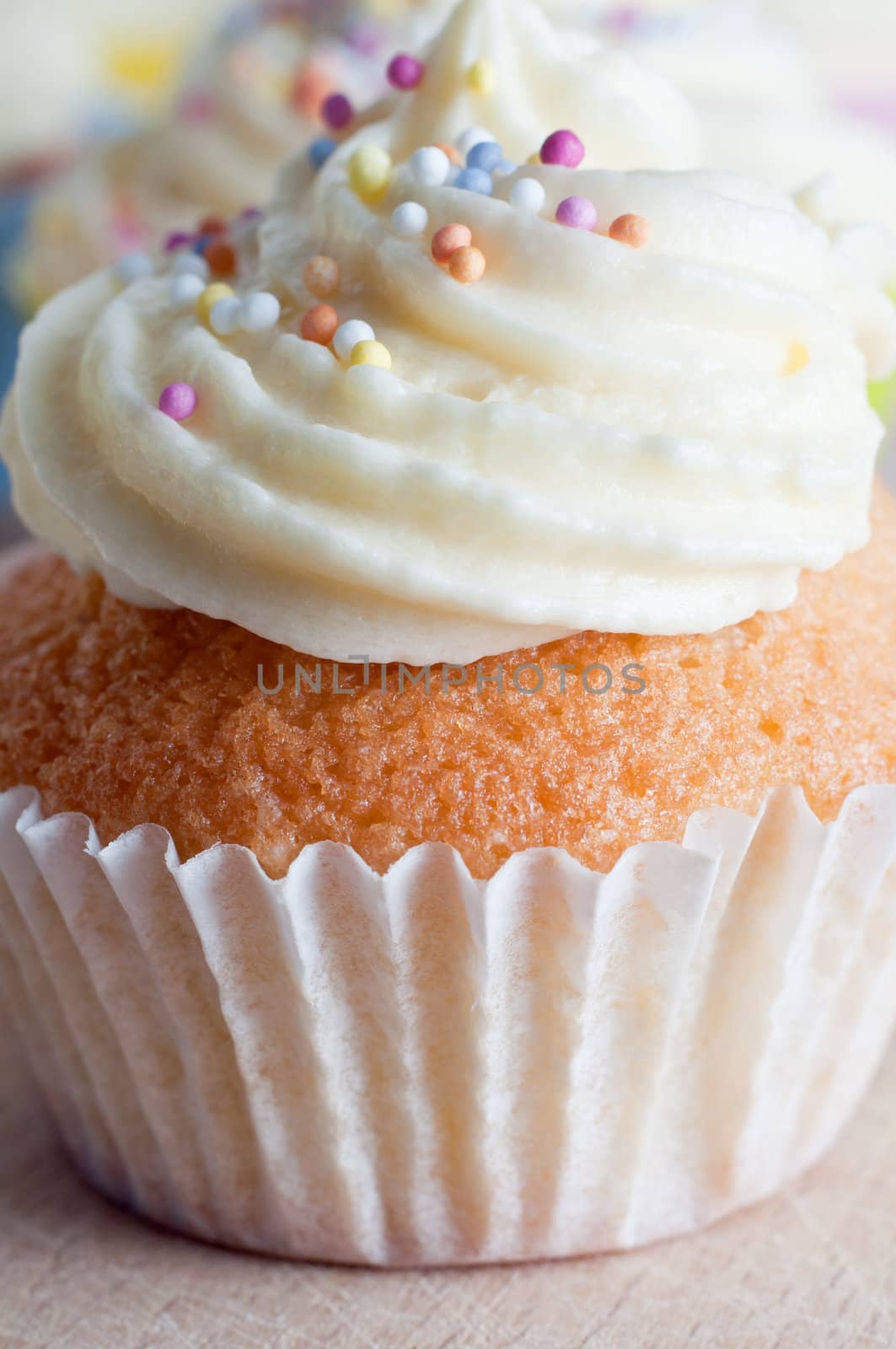 Close up (macro) of a cupcake decorated with a swirl of buttercream icing and colourful sprinkles, photographed on wooden board at eye level.