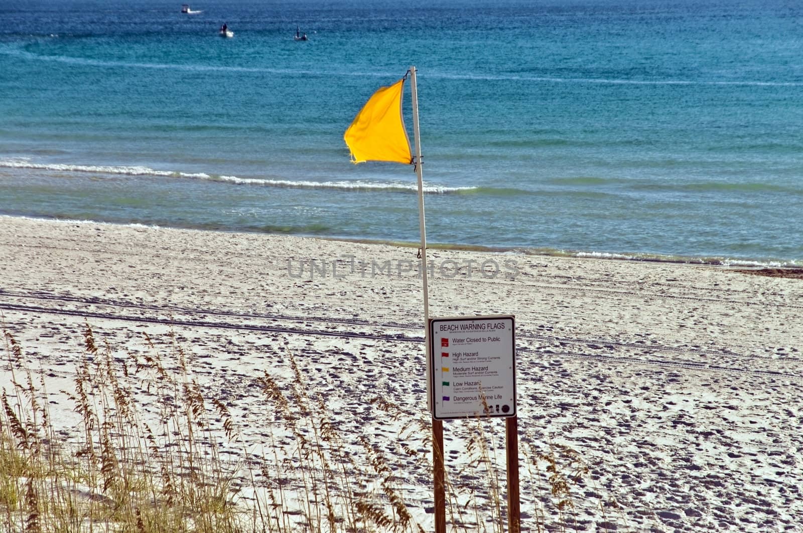 A yellow flag, with sign, waving in the wind on a beach.