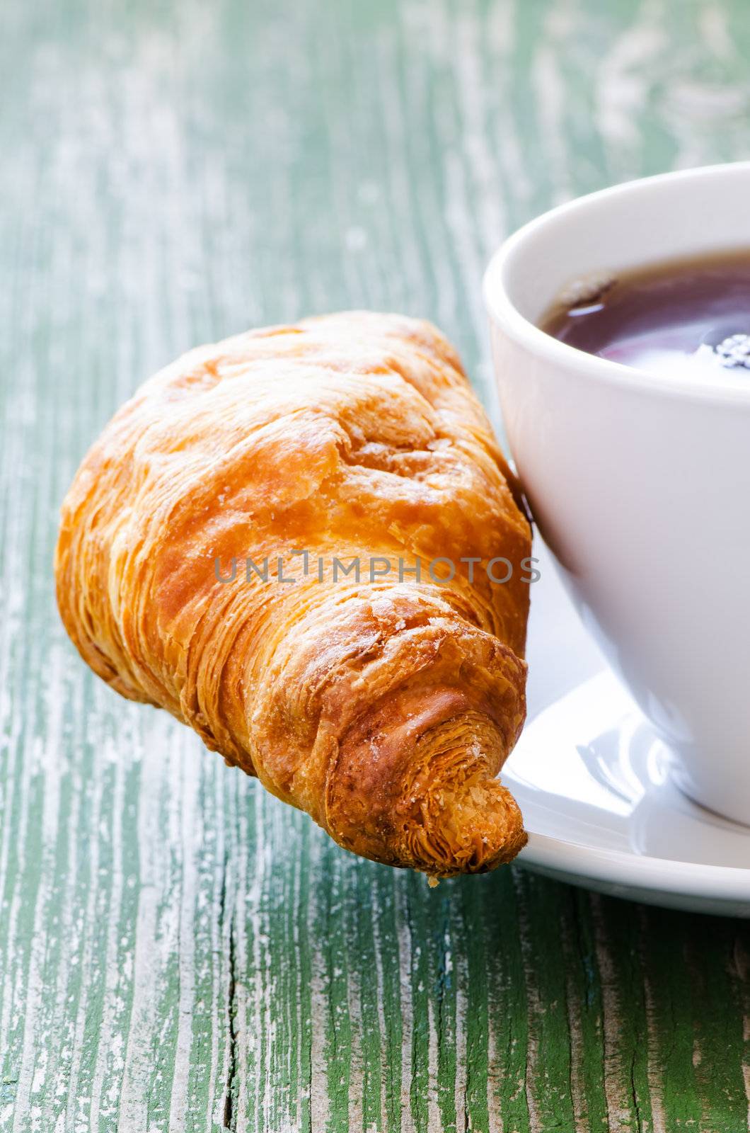 Cup of coffee and croissant on green wooden table