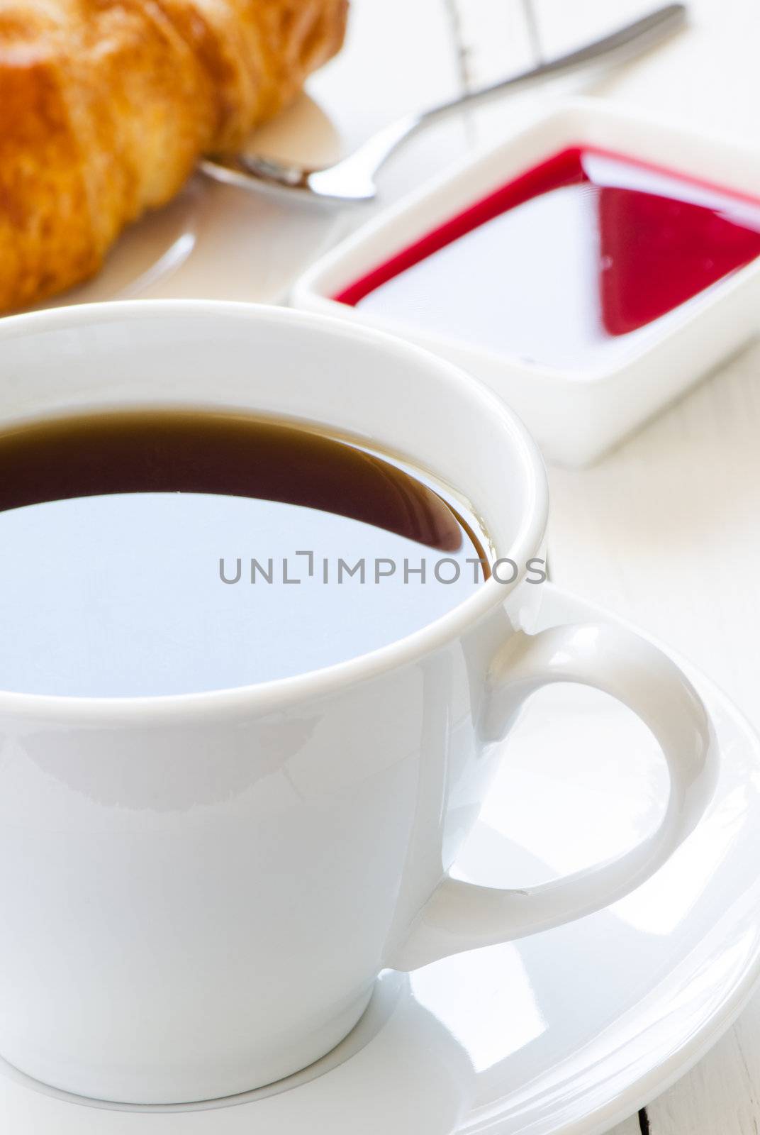 Cup of black coffee with jem and croissant on background