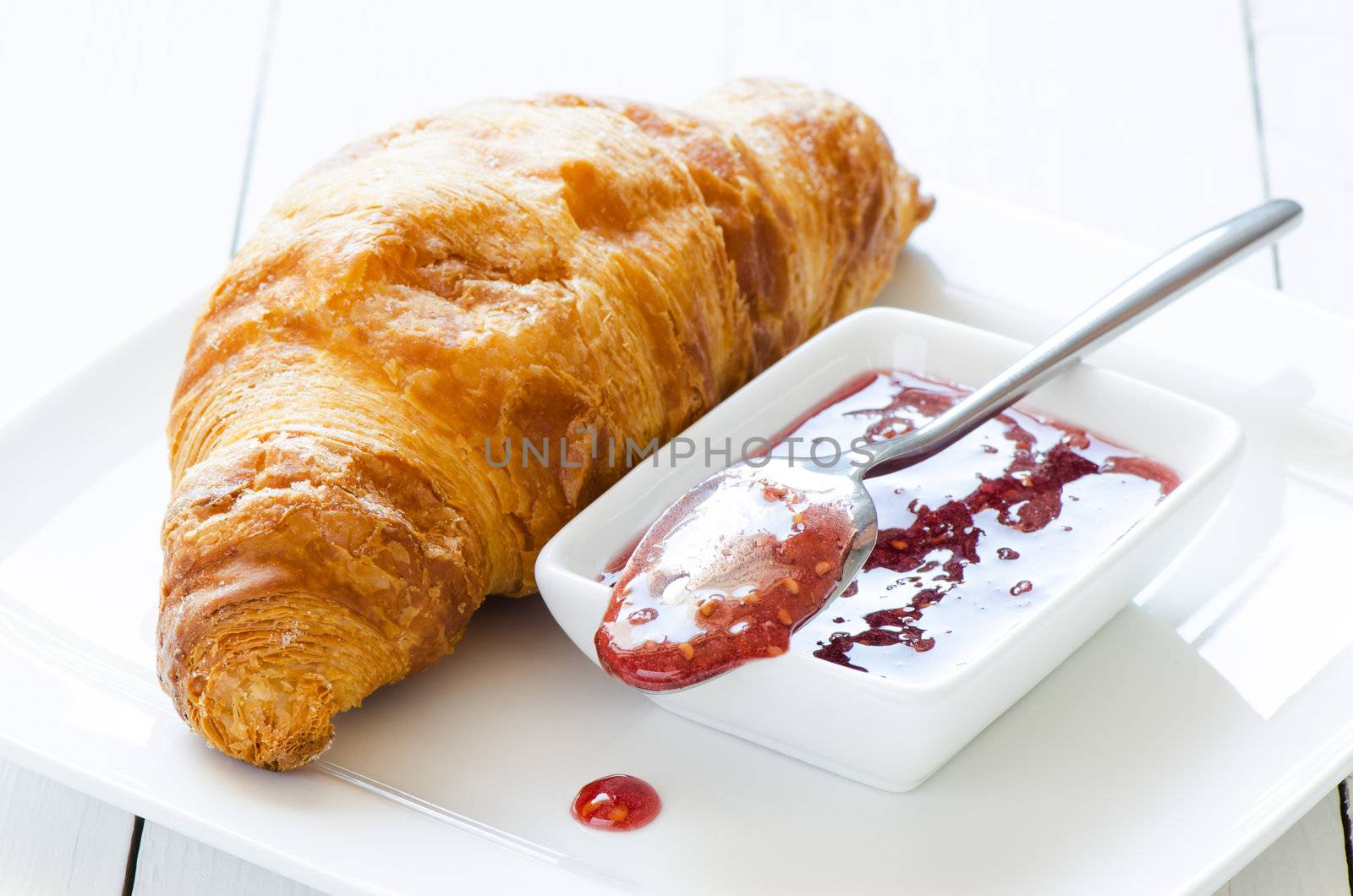 Croissant with raspberry jem on white wooden table