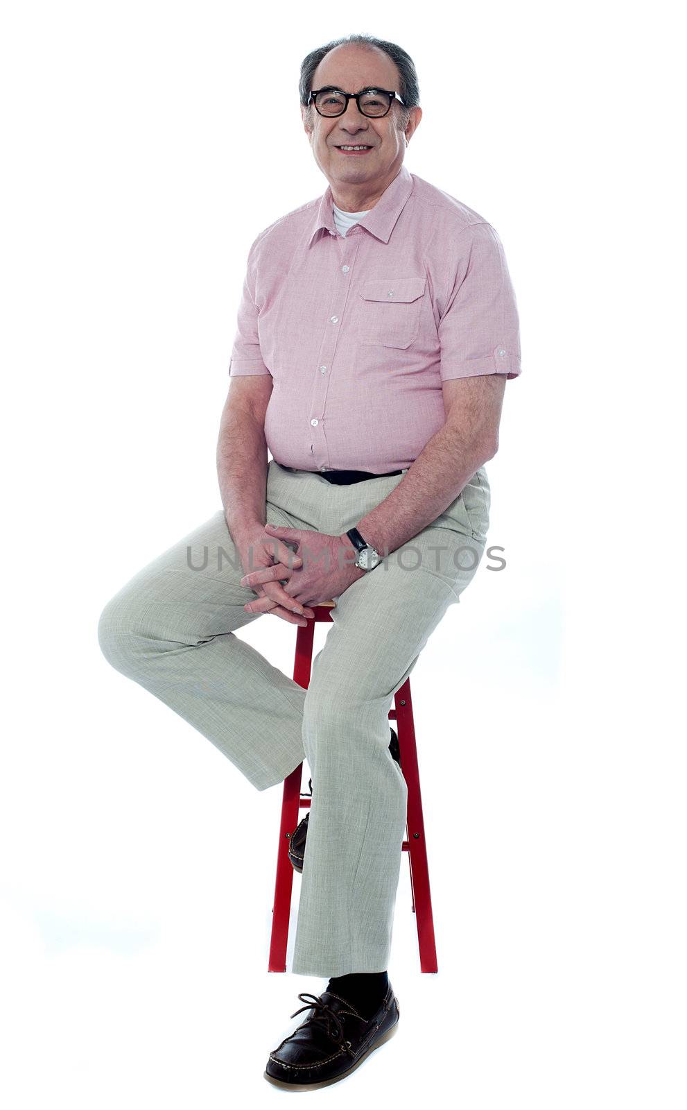 Confident senior man looking at you as he rests on stool, studio shot