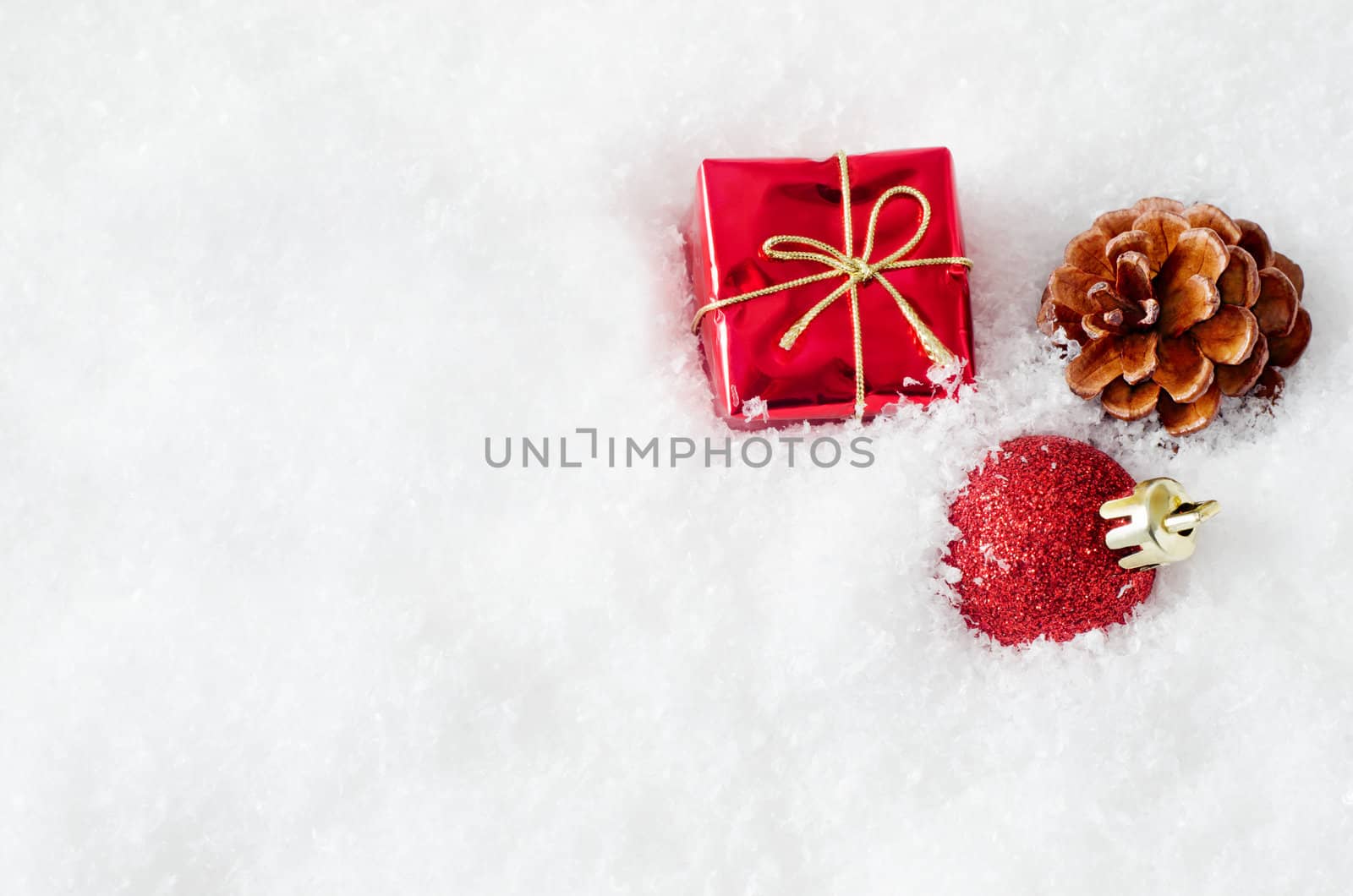 A christmas gift box, bauble and fir cone, embedded in fake white snow to the right of frame, with copy space on the left.