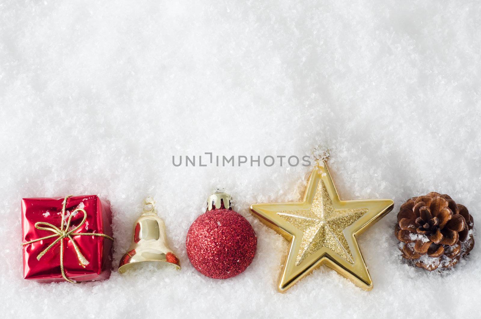 A row of Christmas ornaments, bordering bottom of frame, partially buried in white artificial snow.  Copy space above.