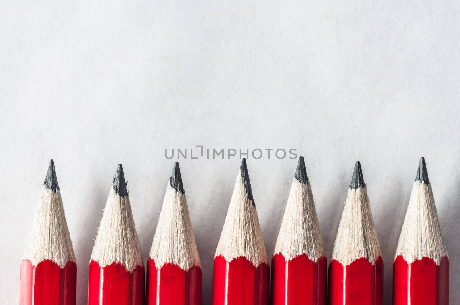 A row of roughly sharpened, grubby red pencils on textured art paper, bordering the bottom of the frame.  Lit and processed to give an old fashioned, vintage appearance.