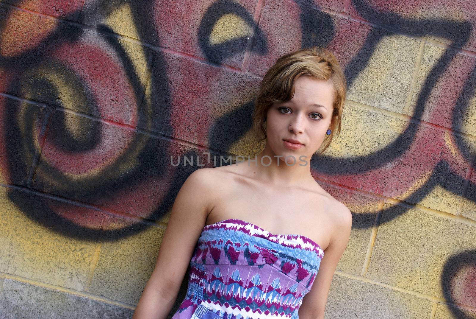 A young attractive woman poses next to some city graffiti.