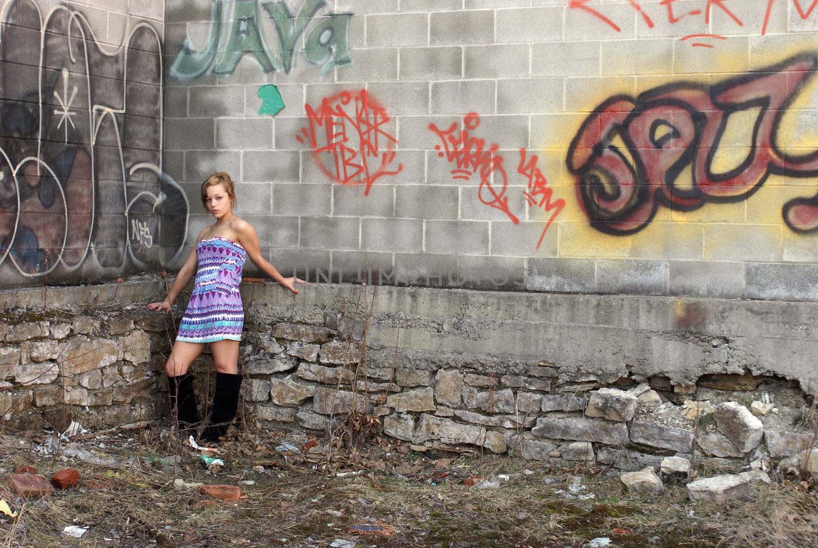 A young attractive woman poses next to some city graffiti.