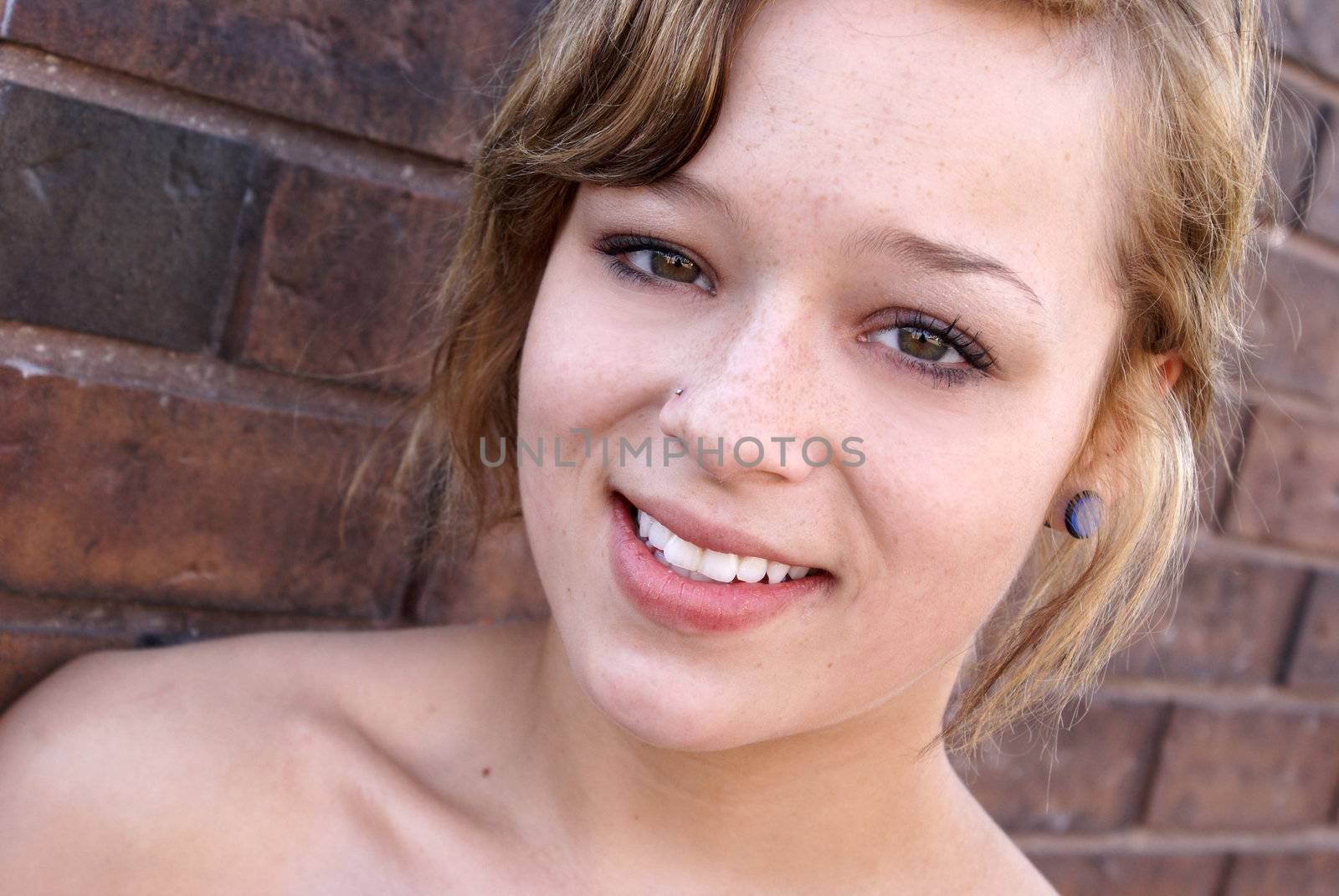 A young woman smiles next to a brick wall in the city.