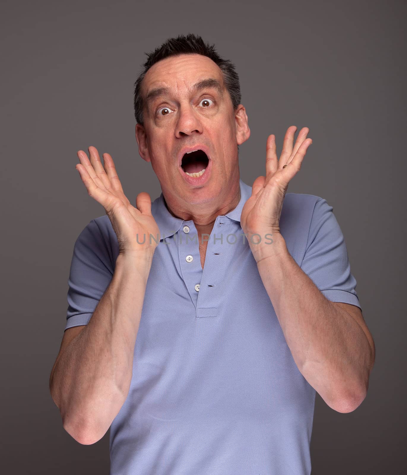 Middle Age Man Screaming in Shock with Hands Raised on Grey Background