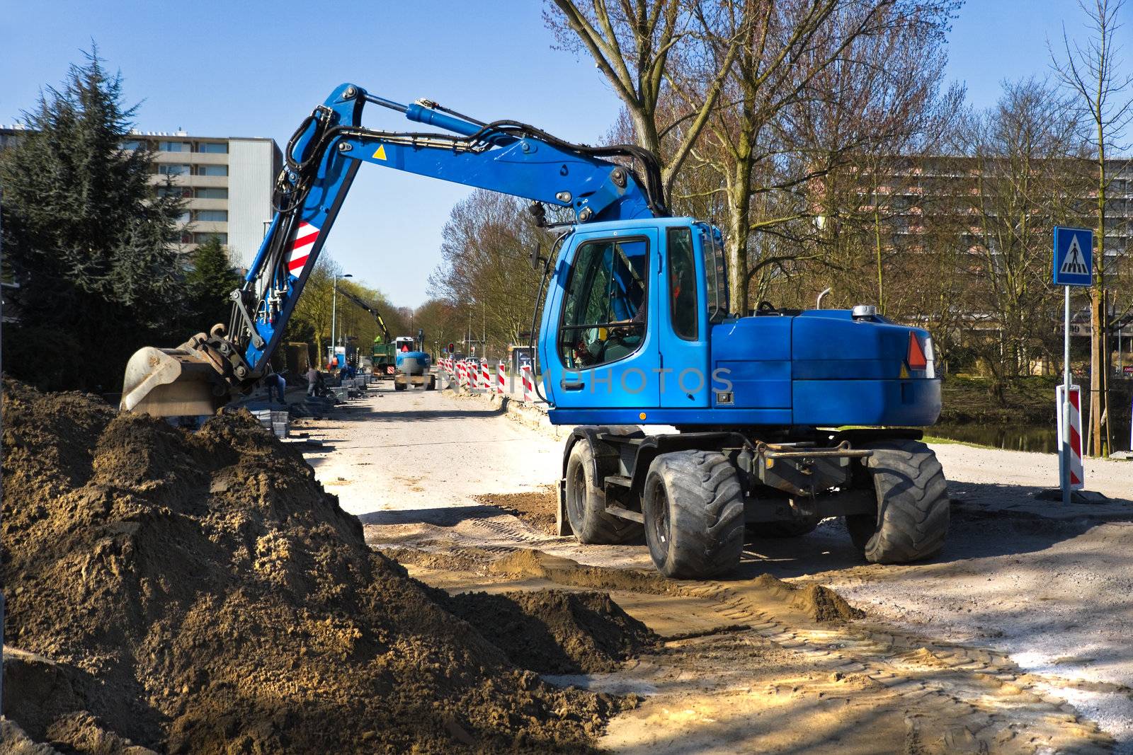 Draglines at work to renew the pavement of a road in the city. Blue excavators and bright blue sky in early spring. Horizontal image.