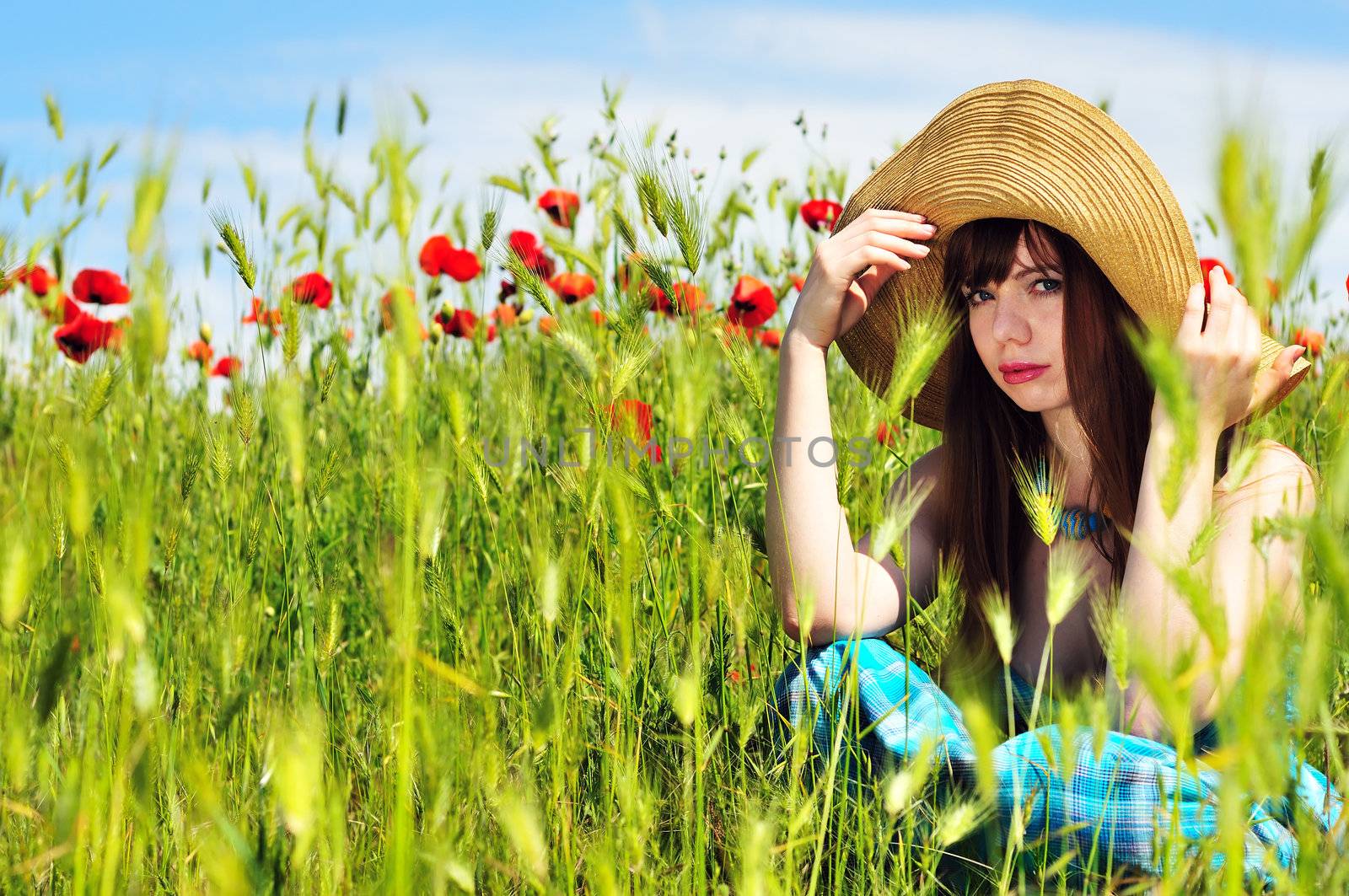 longhaired girl wearing srtaw hat sitting in field