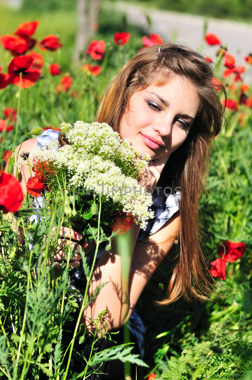 girl with bunch  of wild flowers sitting in the poppy field