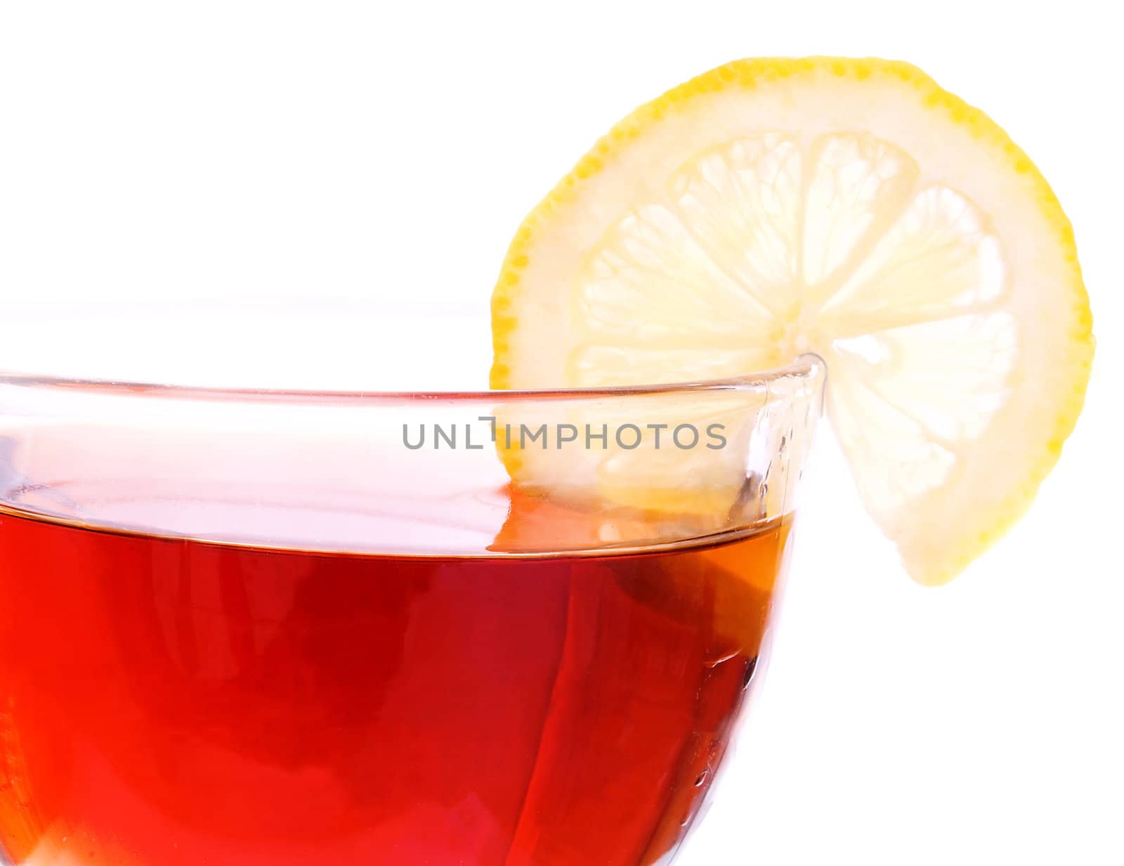 Brim of transparent cup with black tea and segment of a lemon on white background. Focus on right side of the cup.