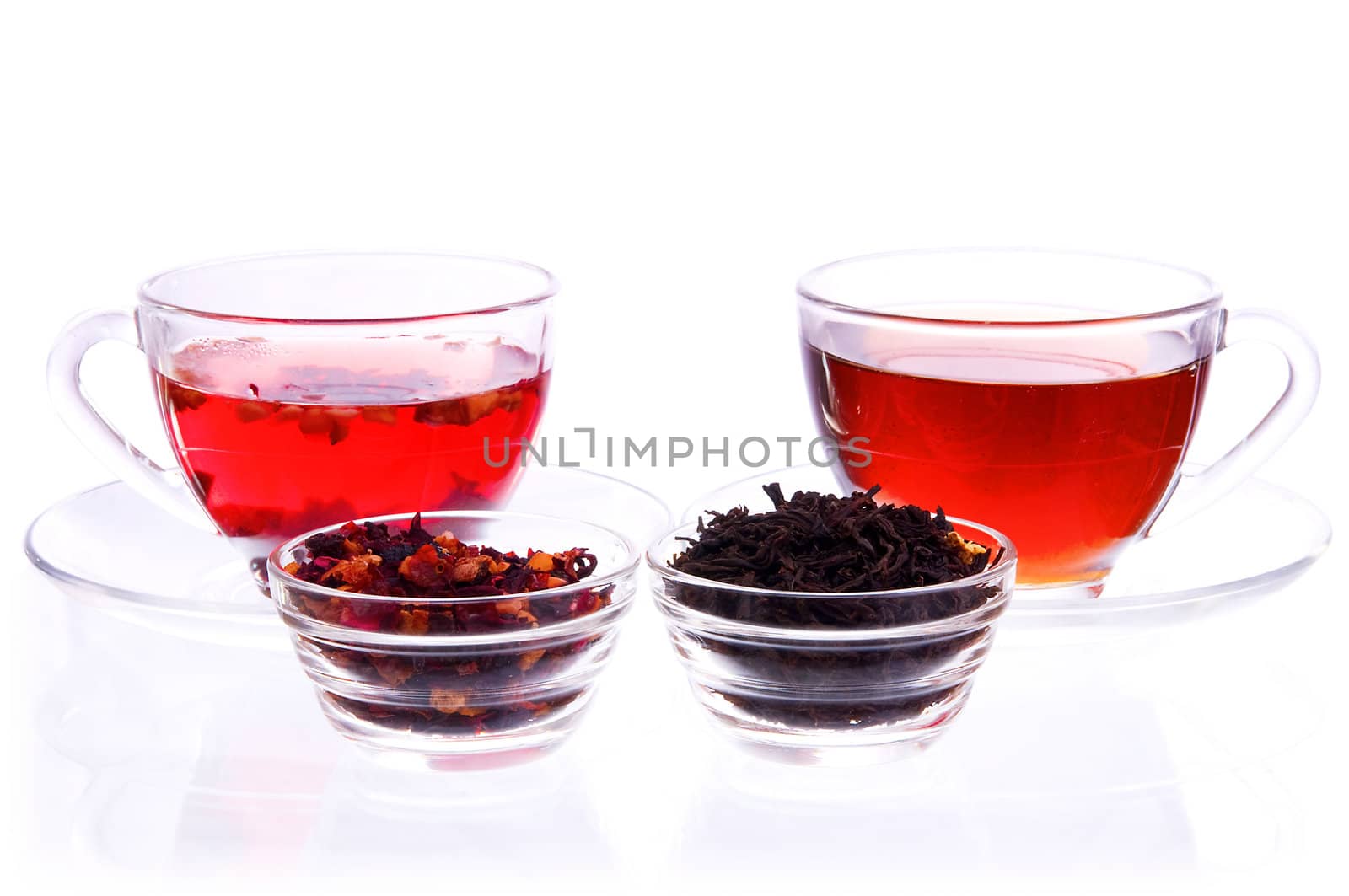 Two transparent cups and saucers with liquid and dry black and fruit tea