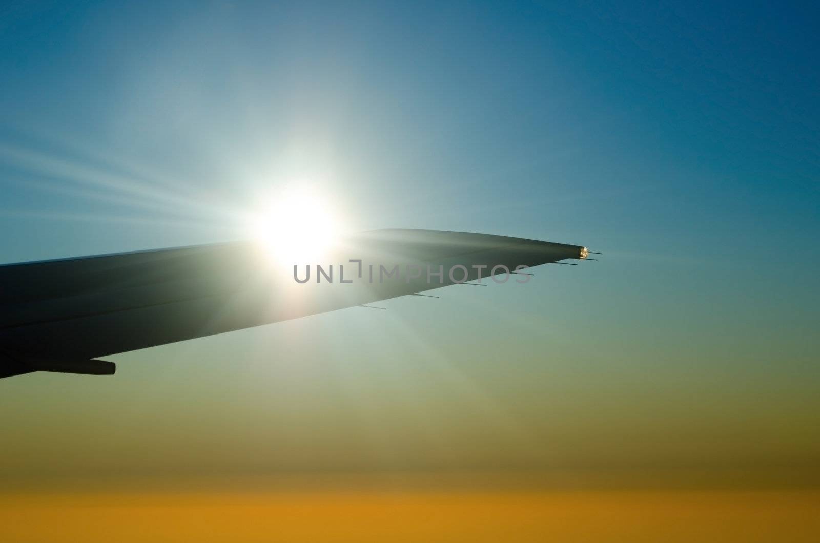 Sun on the airplane wing with many-colored clear sky on background