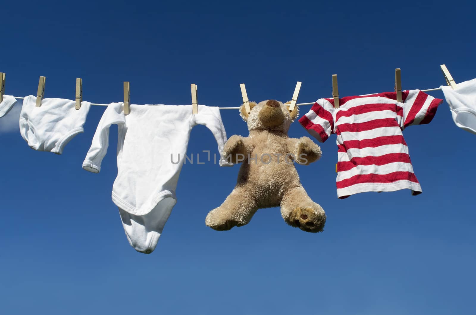 Baby Clothing and a teddybear on a clothesline towards blue sky
