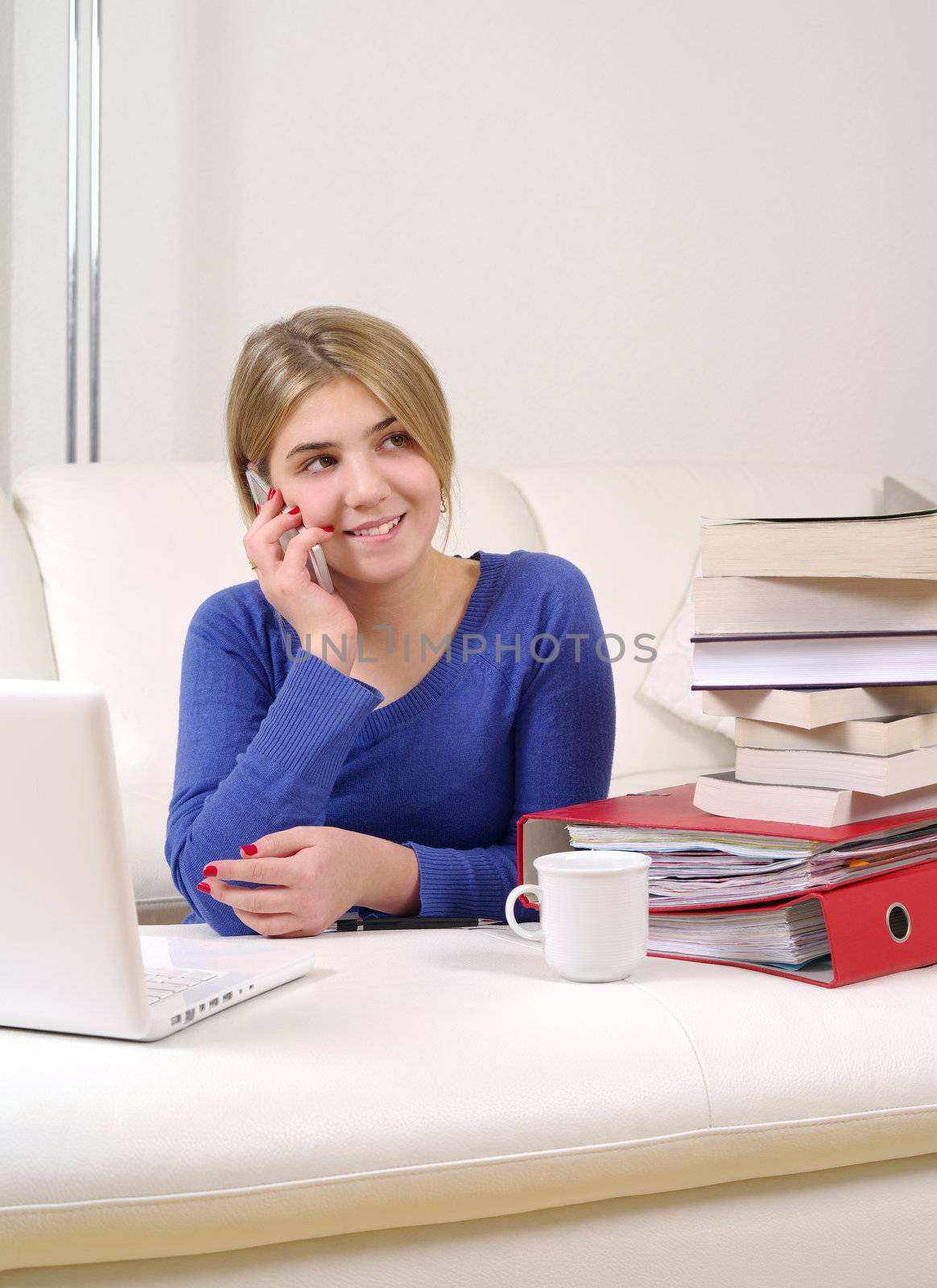 Photo of a beautiful young female sitting and working on a laptop and talking on a smartphone.