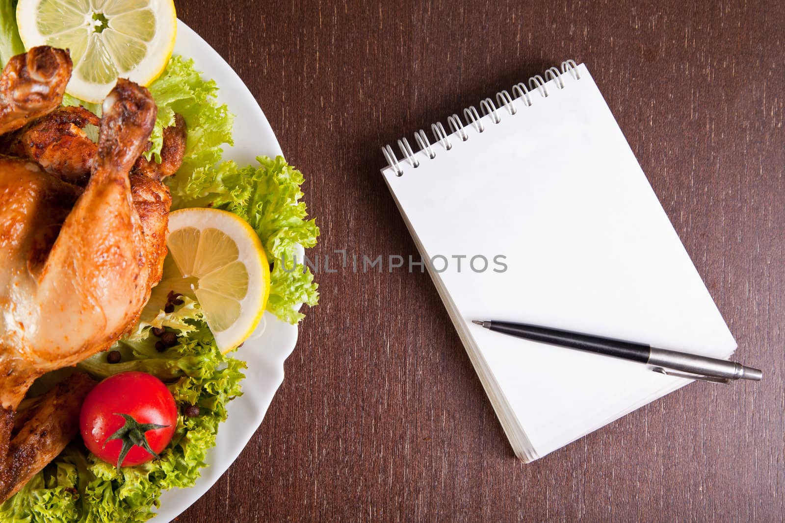 Restaurant table with roast chicken, notebook and pen, ready for order 