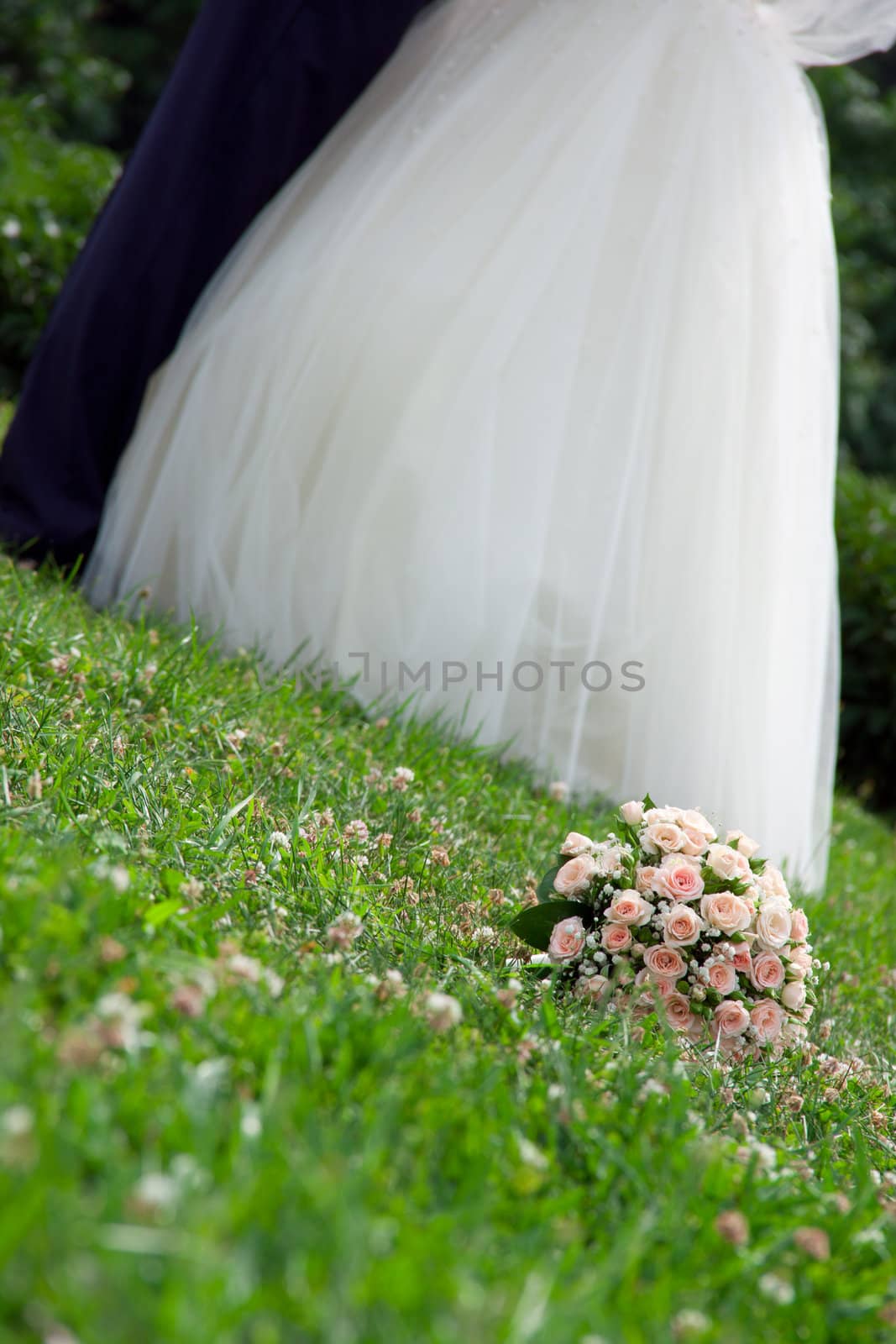 bridal bouquet lies on the grass next to the bride and groom are kissing