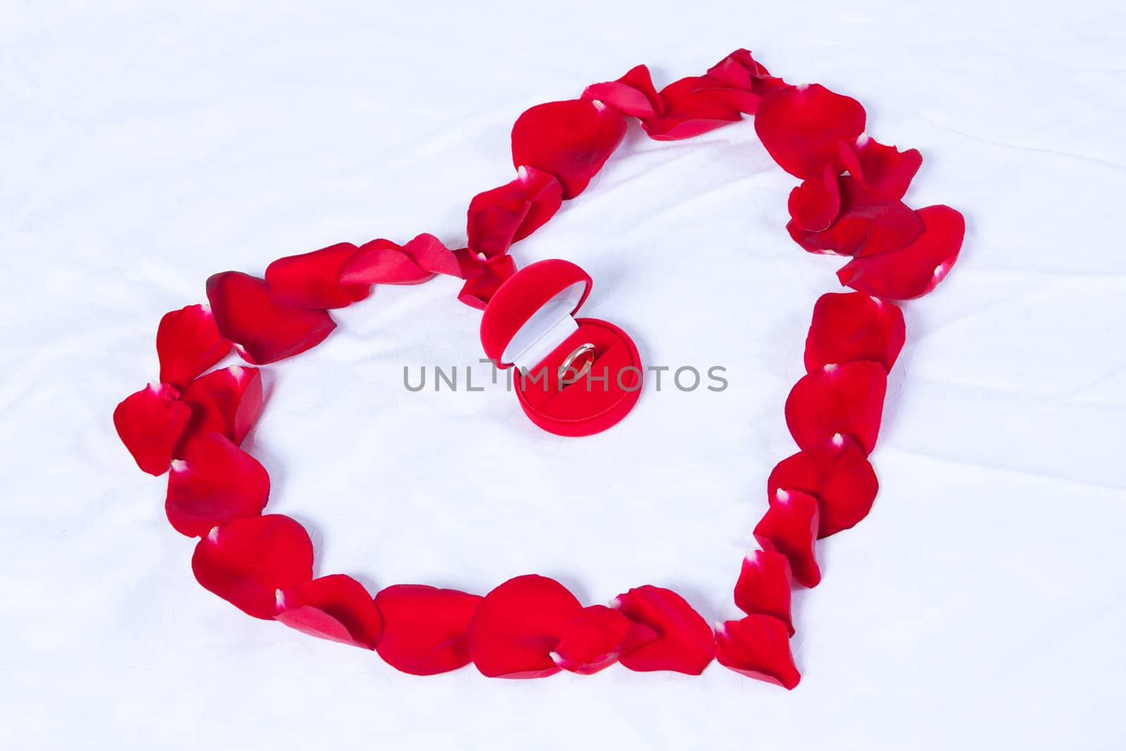Wedding rings in the red box lie on the bed in the heart of rose petals