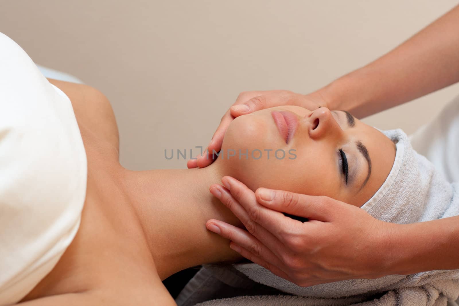 young woman in a spa salon lays on a table and receives a facial massage.