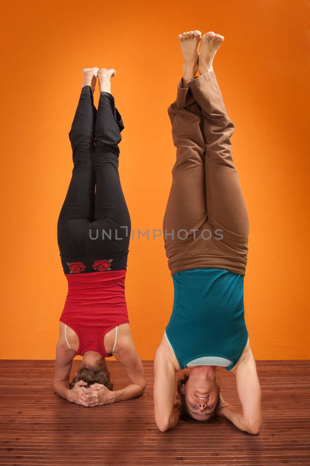 Two women perform Sirsasana headstand positions over orange background