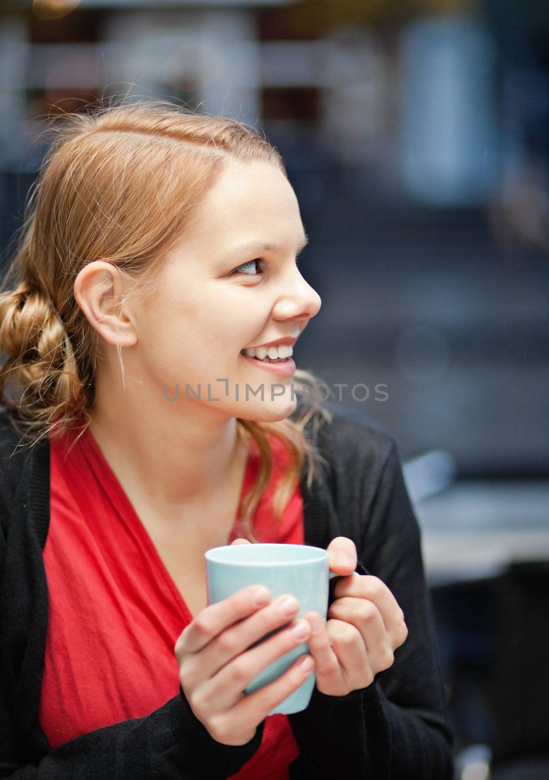 Pretty young woman holds a cup of hot drink in a restaurant outdoors