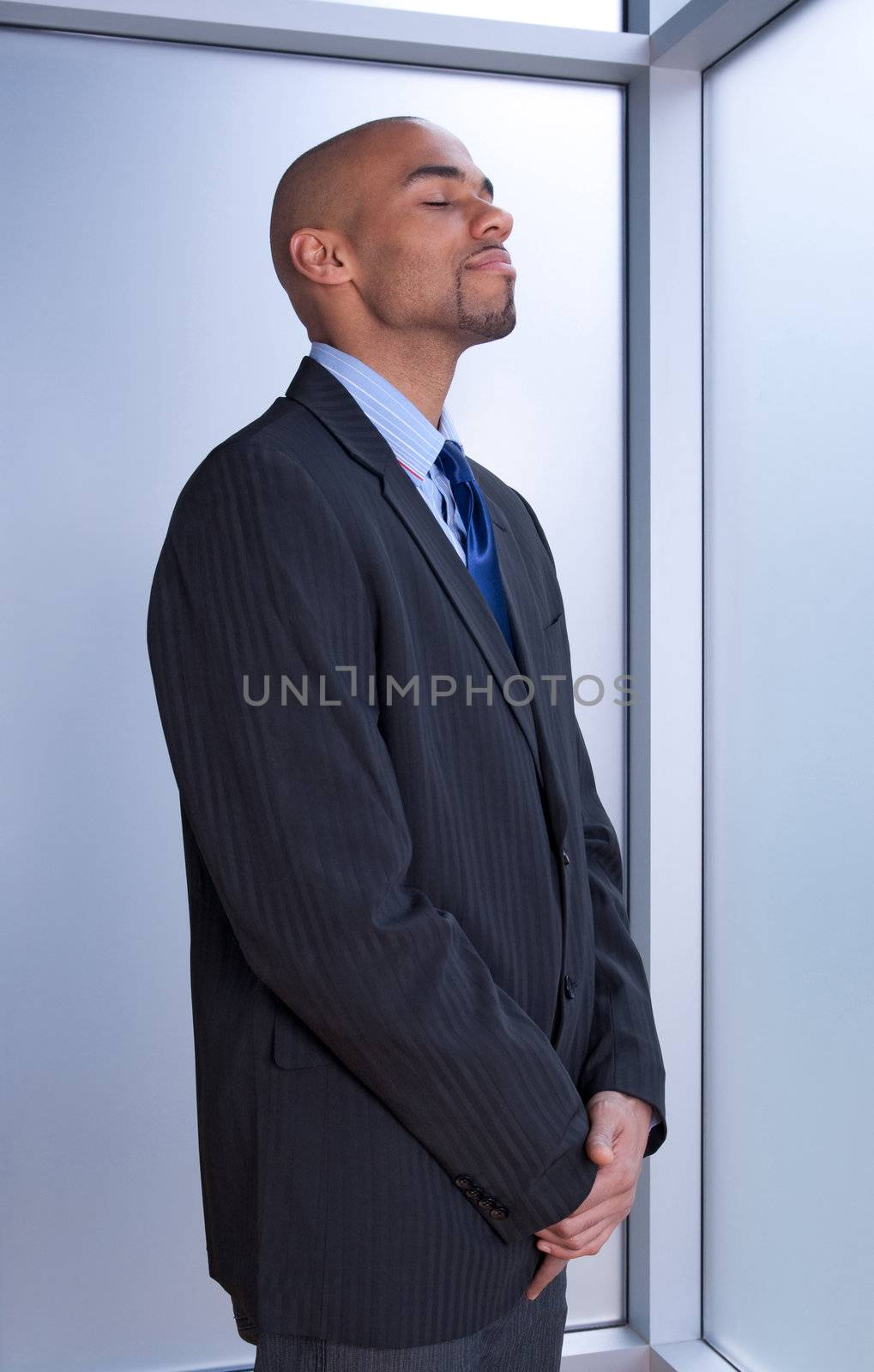 Businessman looking zen, standing with his eyes closed near a window.
