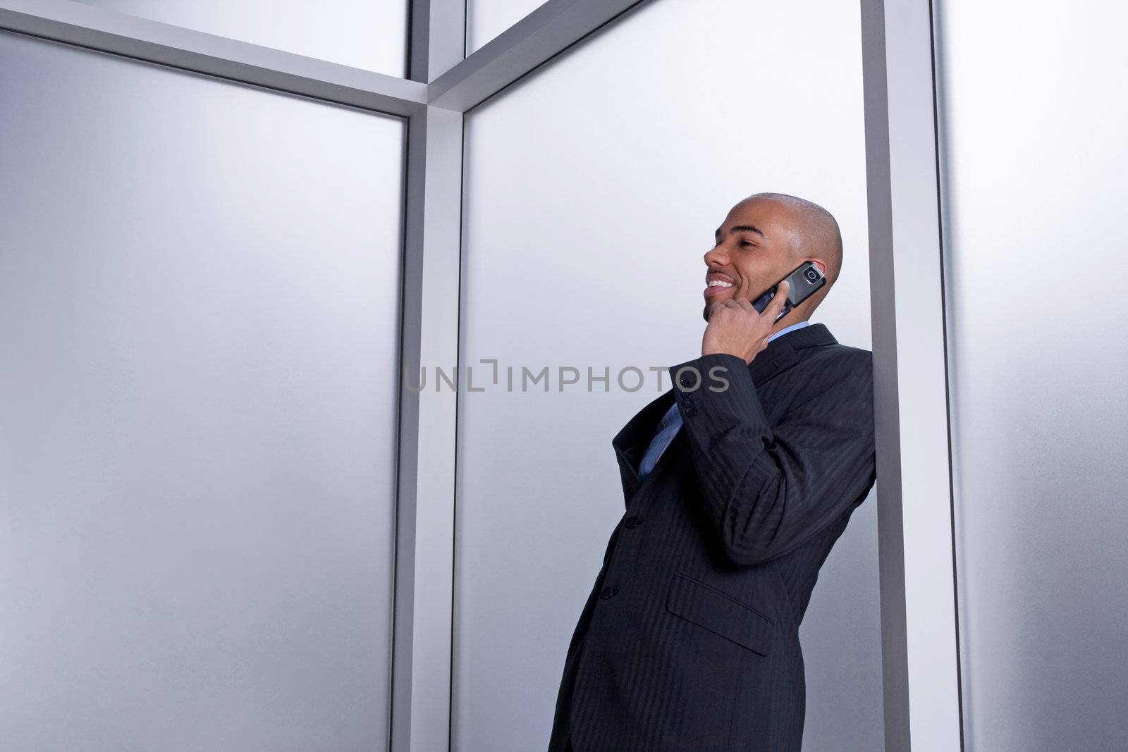 Businessman talking on his cell phone and smiling, beside an office window.