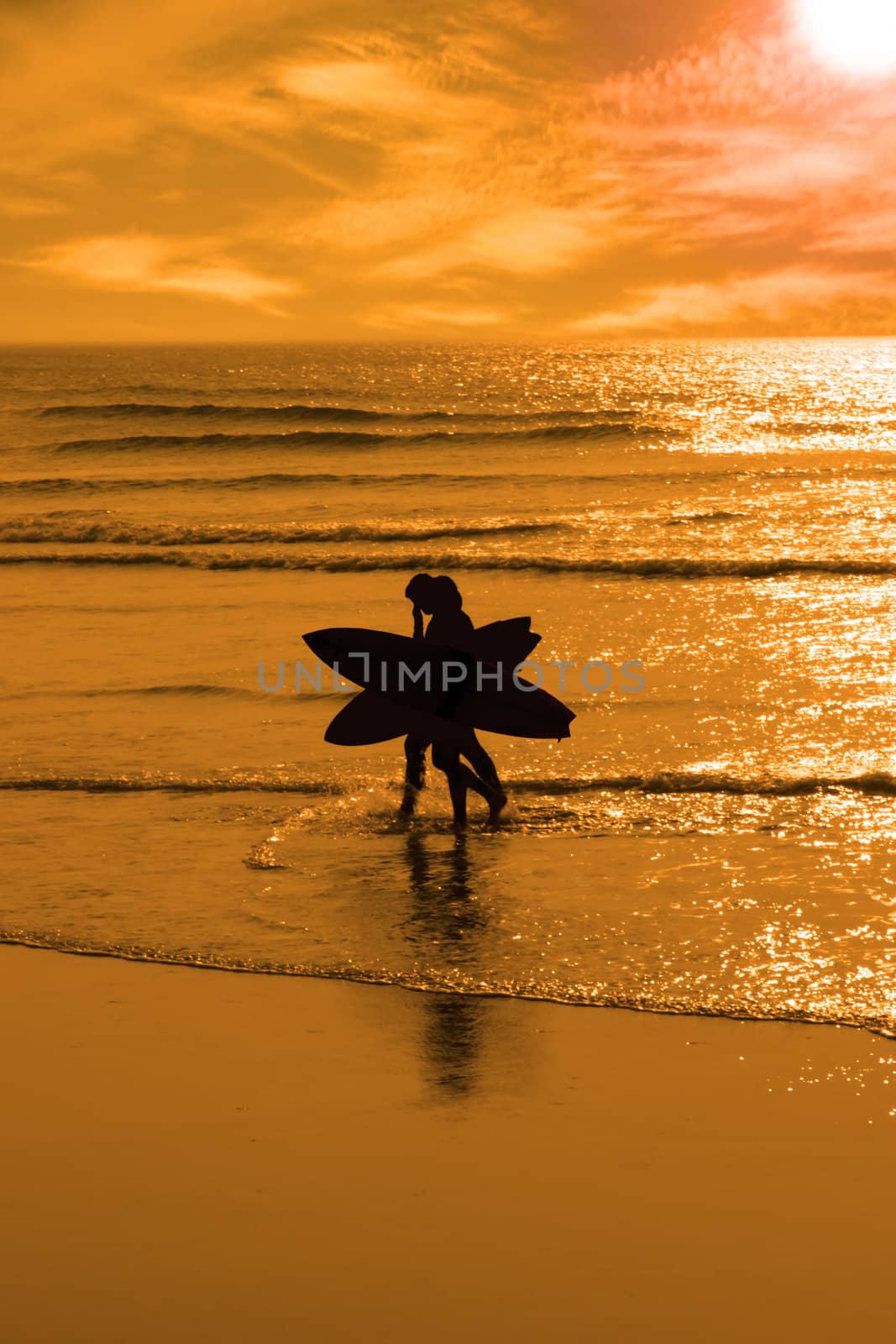 silhouette of surfing couple walking from the sea to the beach just before sunset with silhouette in shape of an angel or x