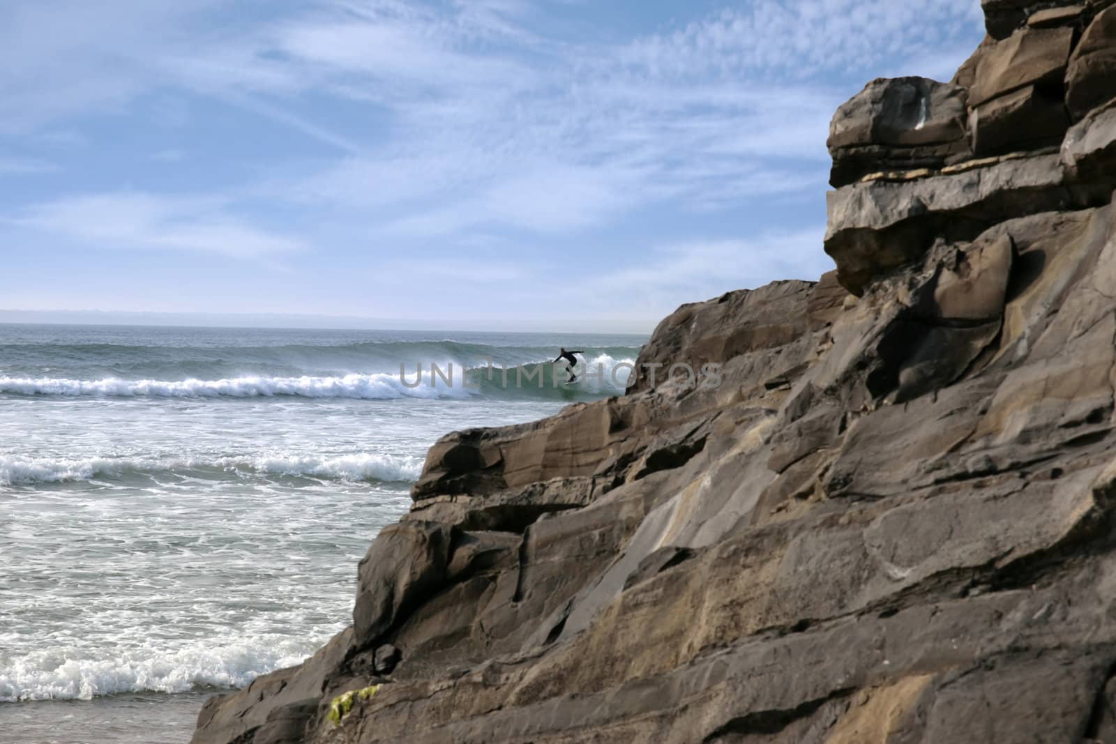 beautiful clean atlantic ocean with lone surfer catching the waves with cliffs and rocks in foreground on Irelands coast