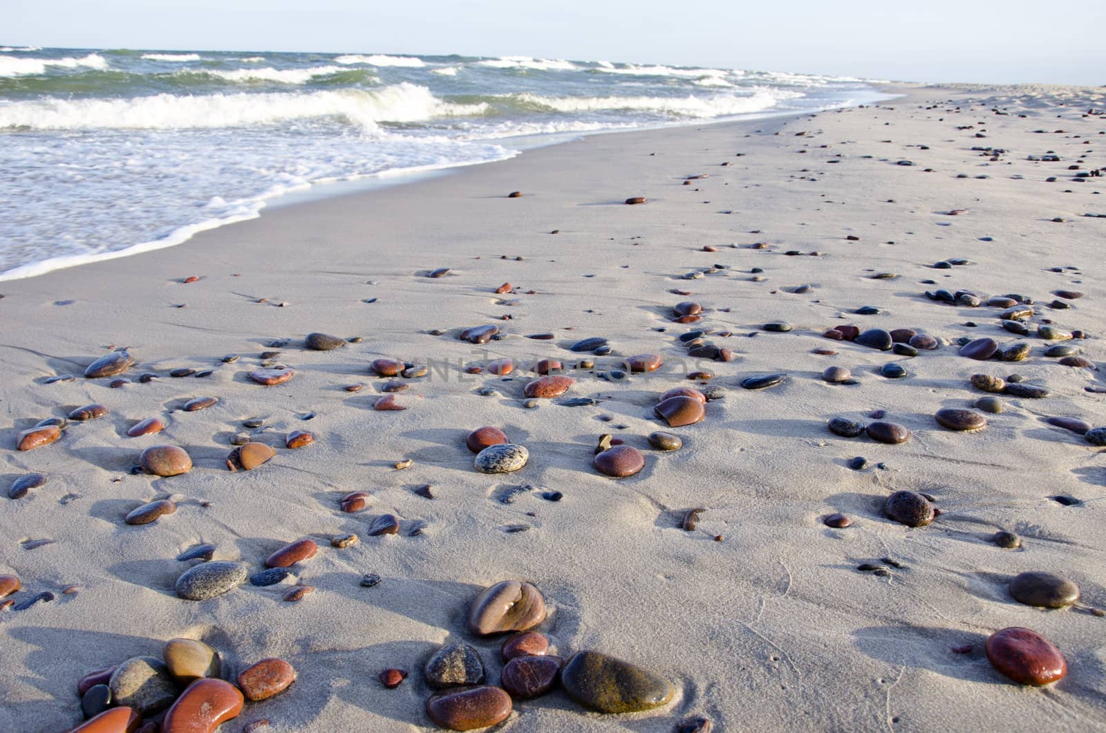 background of seashore little stones beautiful reflections of sun. sea waves beating coast with sand.