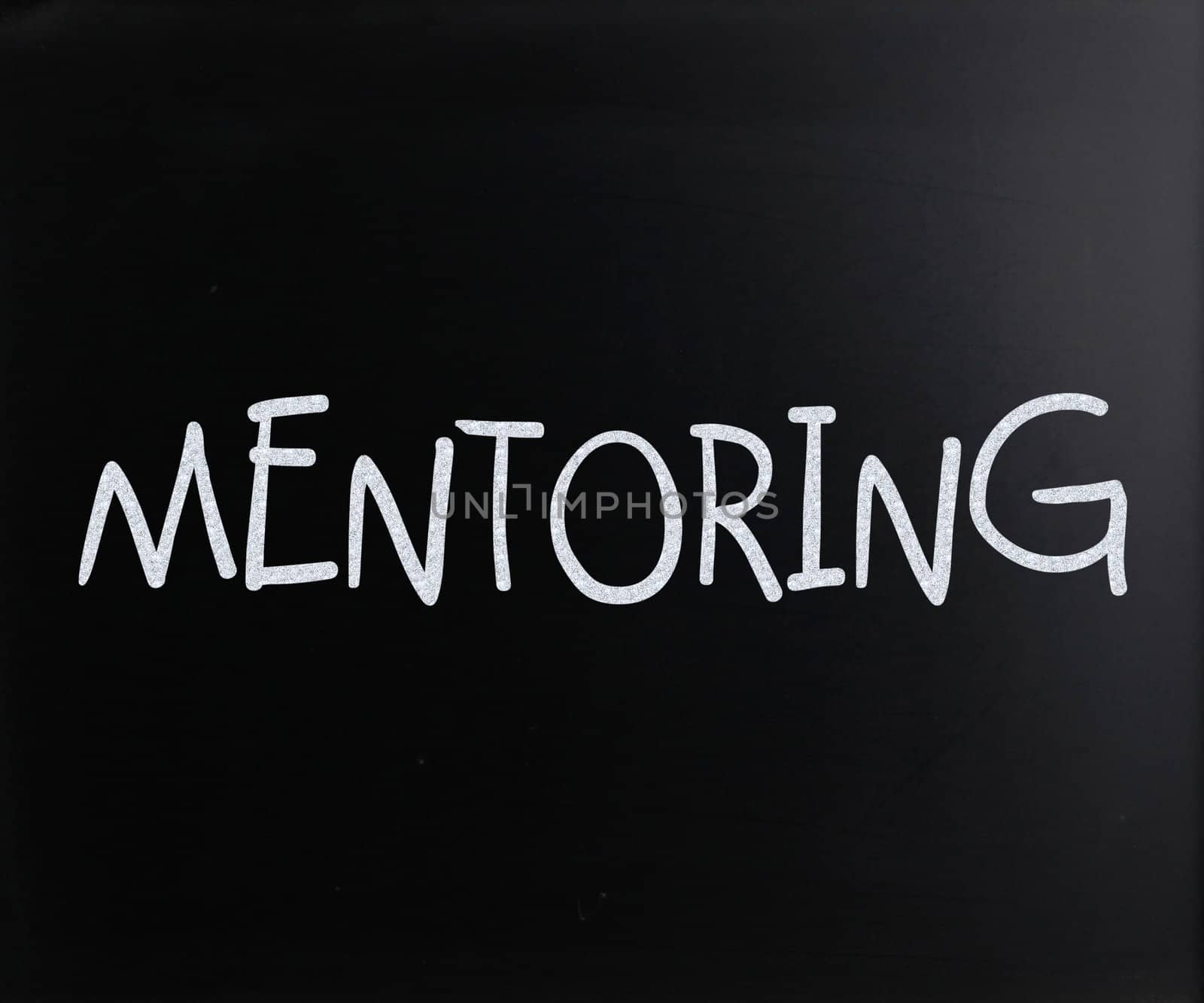 The word "Mentoring" handwritten with white chalk on a blackboard