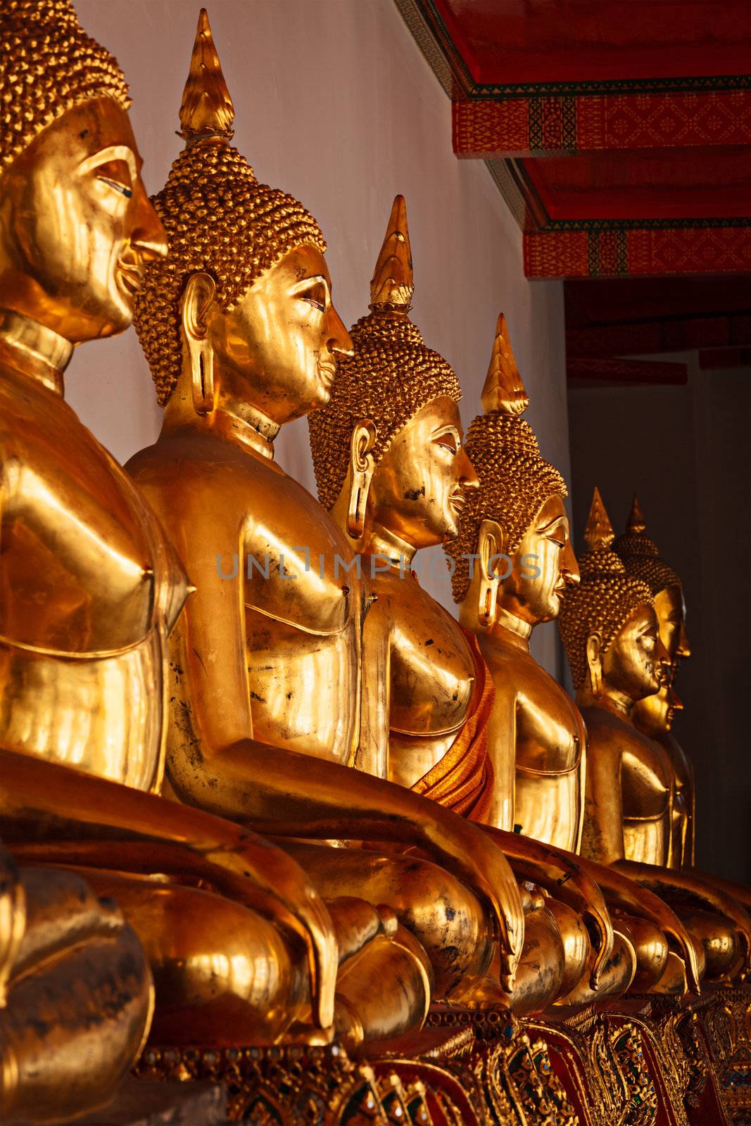 Row of golded sitting Buddha statues in Buddhist temple Wat Pho, Bangkok, Thailand. Low point of view, focus on 3rd one from the left
