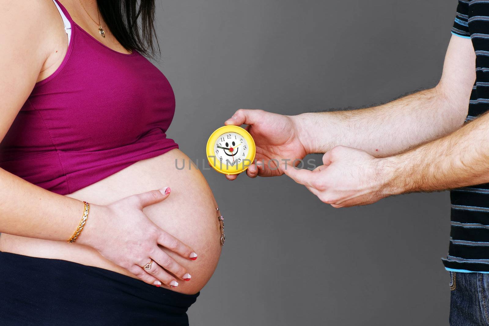 Funny pregnancy concept of dad showing the time to his pregnant wife's belly, implying that it is time to give birth.